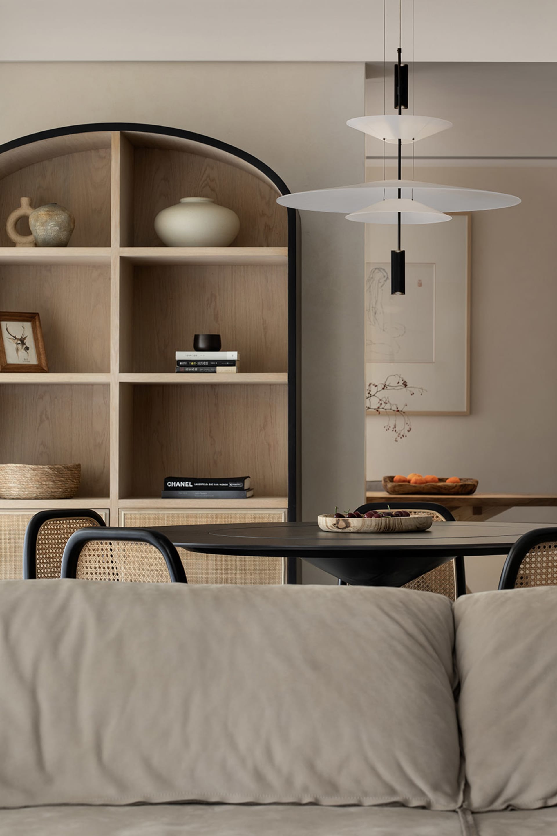 Modern minimalist dining room featuring a round table with wicker chairs, a wooden shelving unit, and a pendant light fixture