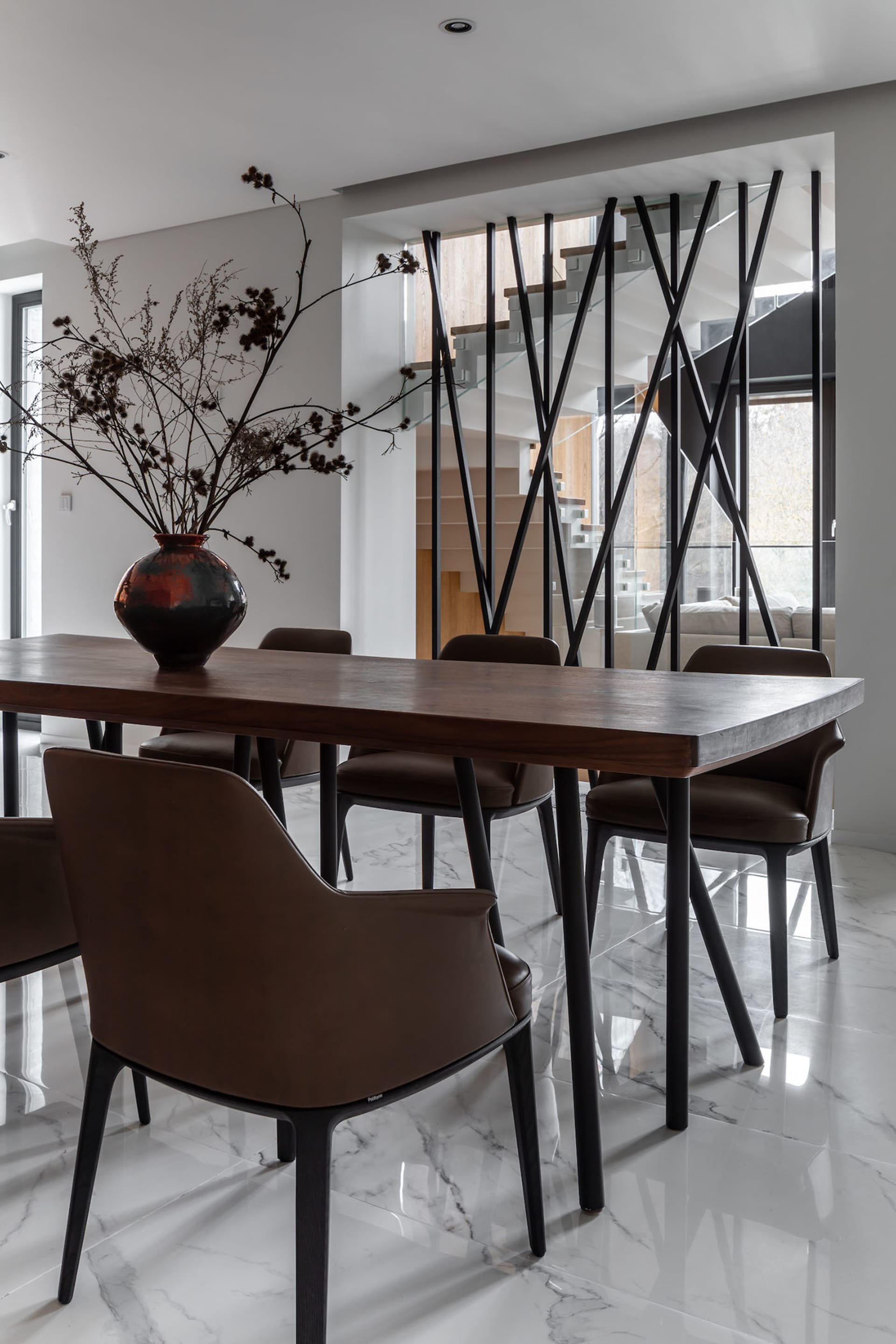 A modern dining room with wooden table, leather chairs, glass vase, and minimalist design.