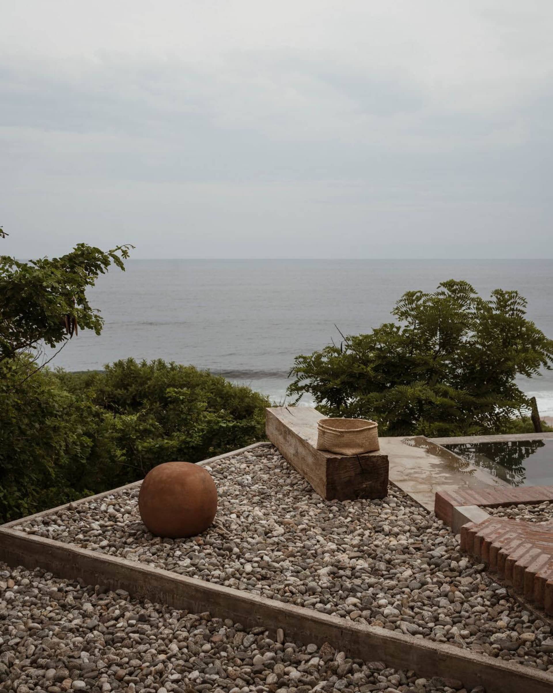 A granite patio with a view of the ocean, featuring a wooden bench, a spherical object, and a woven basket.