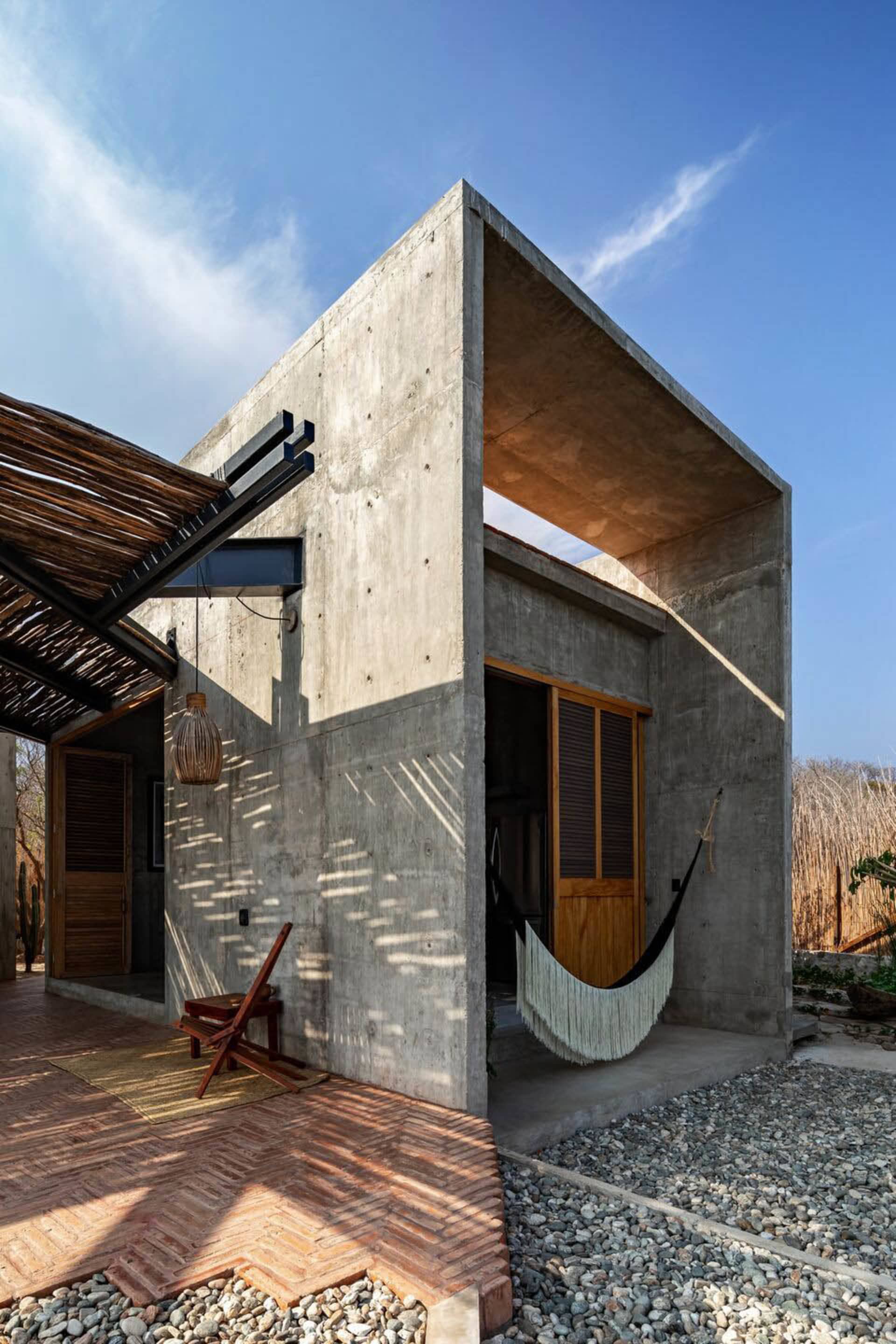 A modern house with concrete exterior featuring a hammock and a wooden door.