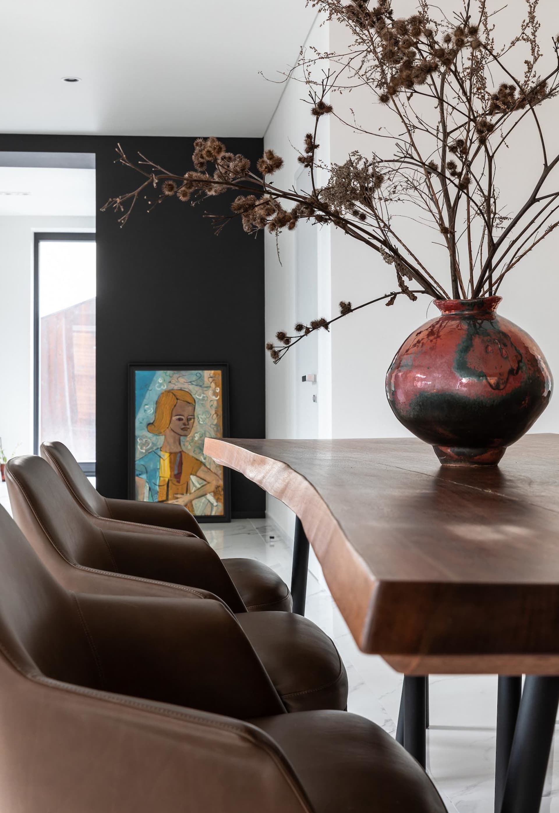 A modern dining room featuring a wooden table adorned with a large, decorative vase filled with dried flowers, and three brow