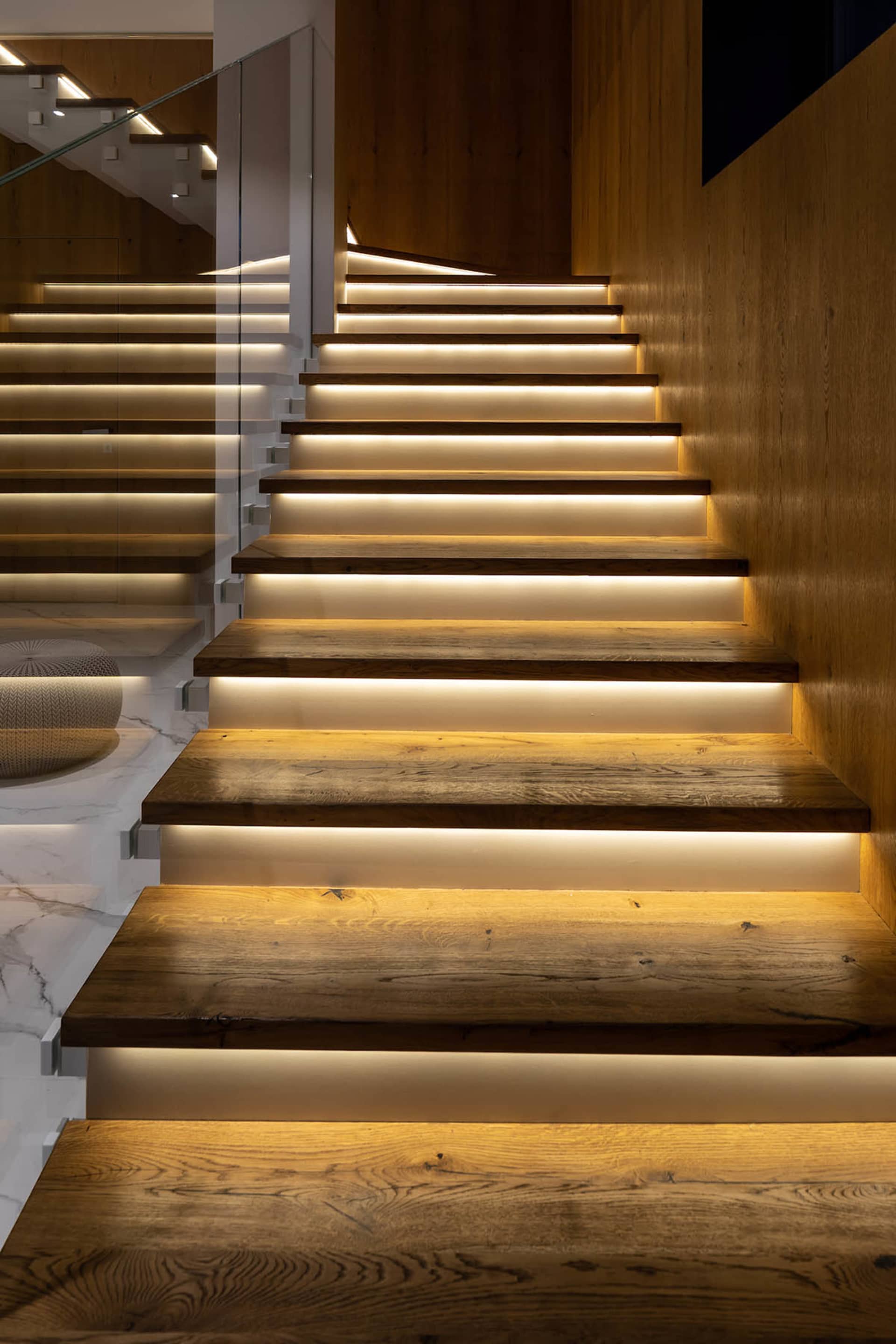 A modern staircase featuring wooden steps with recessed lighting on the underside of each tread for illumination.