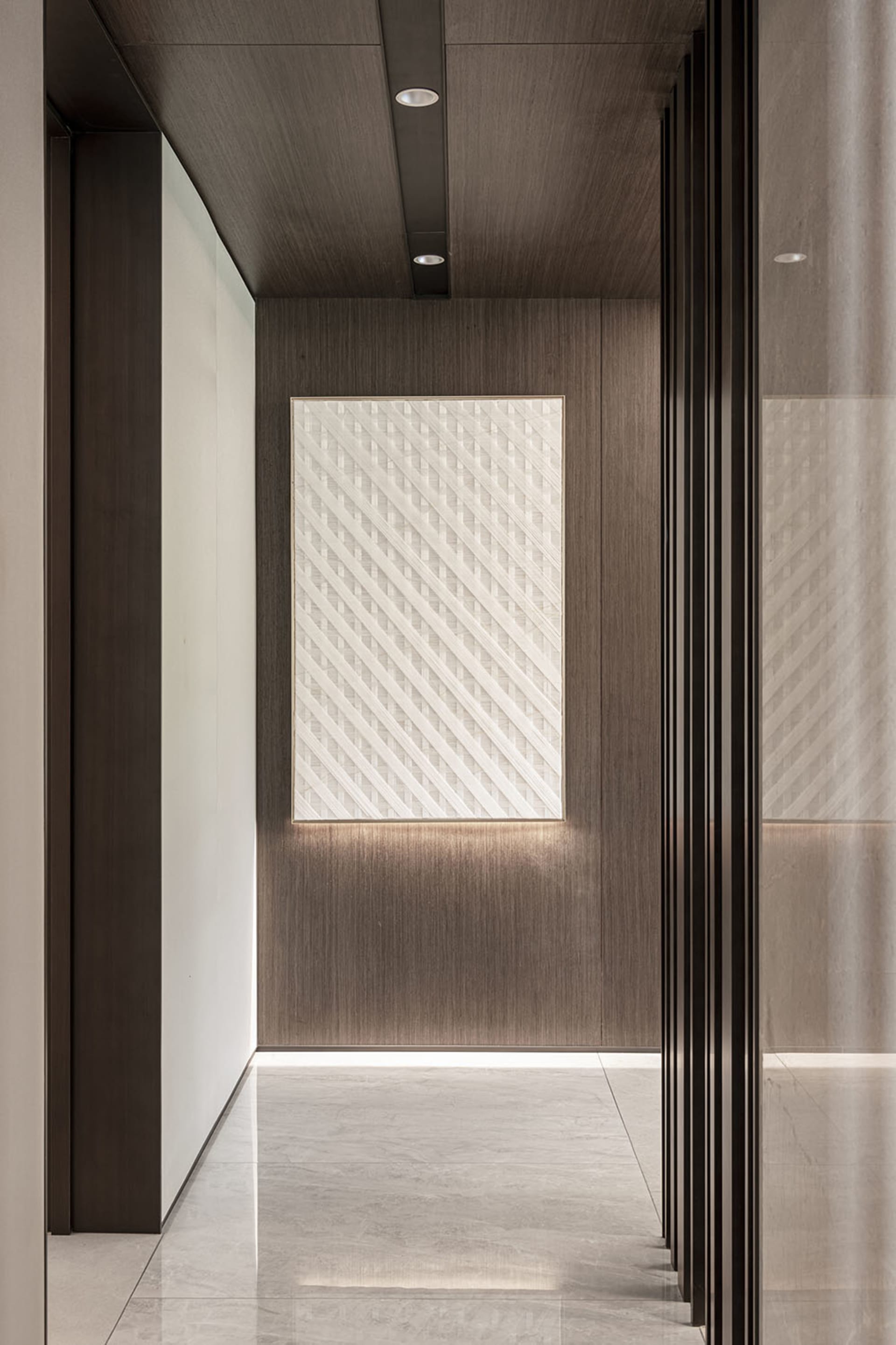 A modern corridor featuring a paneled wall with diagonal lines, illuminated by concealed lighting.