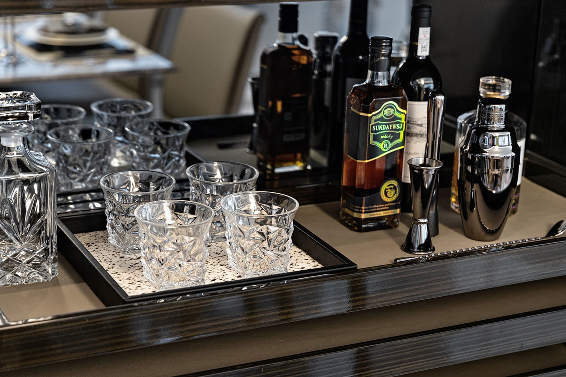 A sleek, modern bar counter featuring polished glass and ceramic materials, with various bottles and glasses neatly arranged.