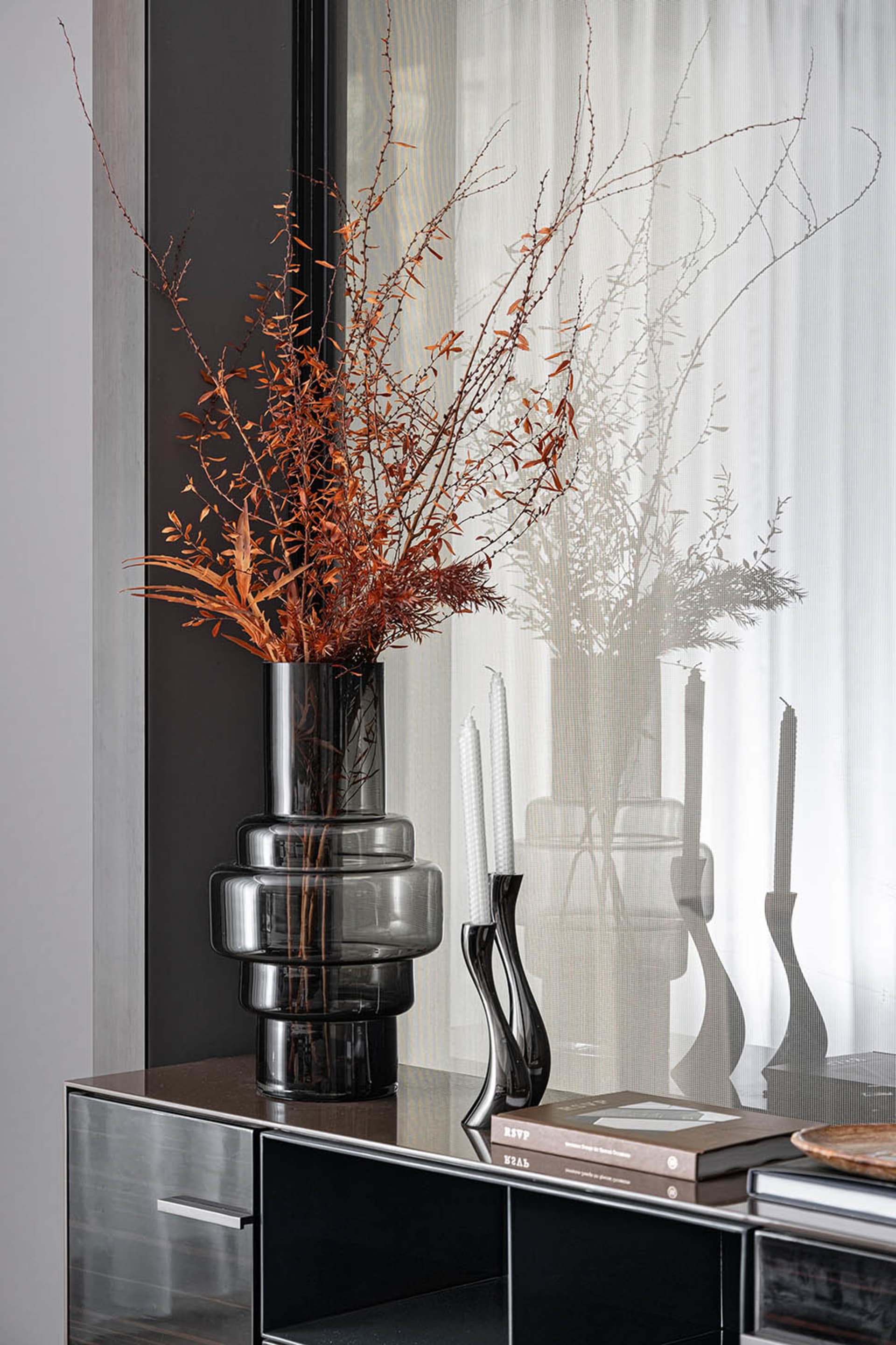 A modern shelf decorated with a tall black vase containing dried flowers, a black bottle, and books.