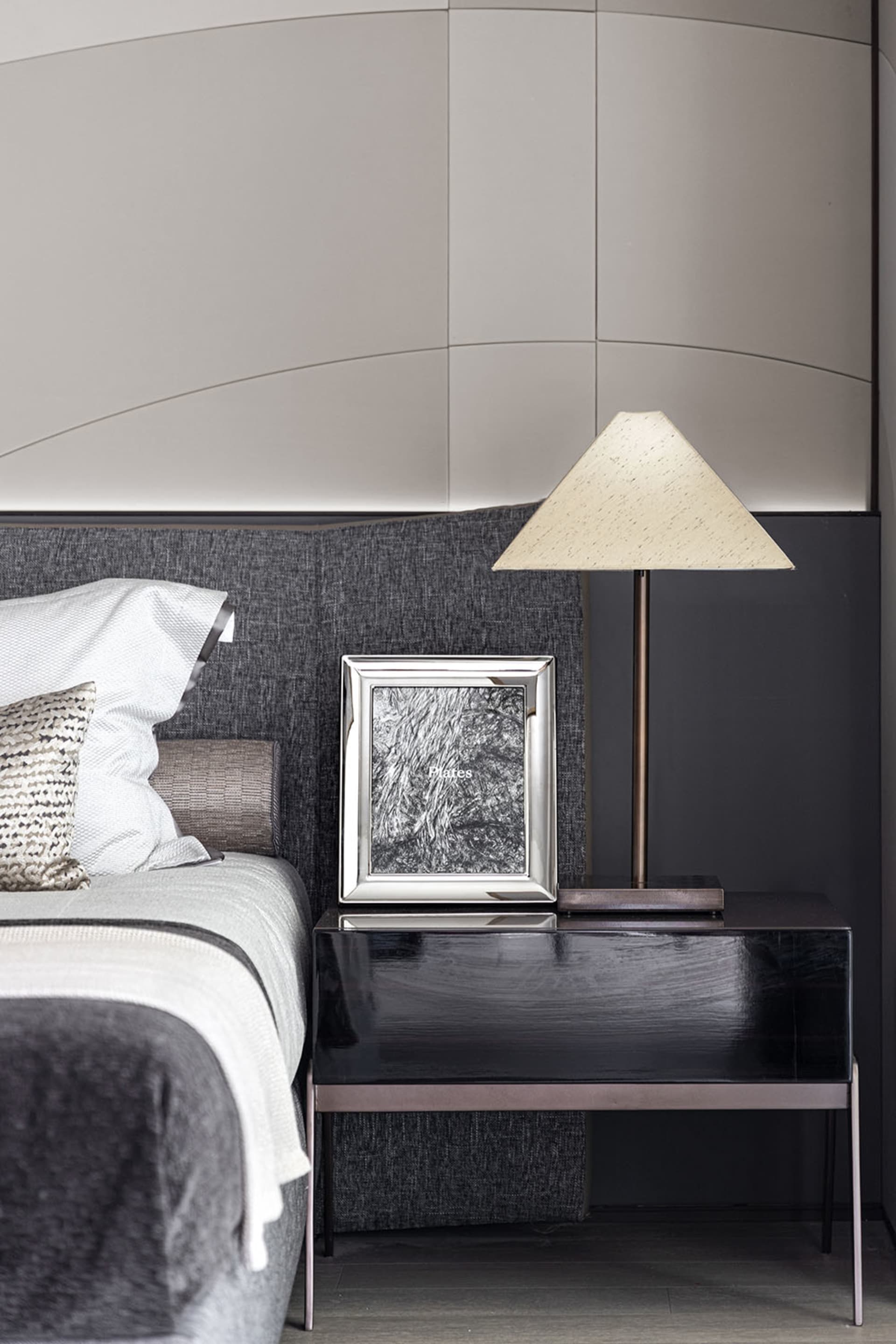 A modern bedroom featuring a black side table with a white lamp, a white bed with a black headboard, and a black and white pi