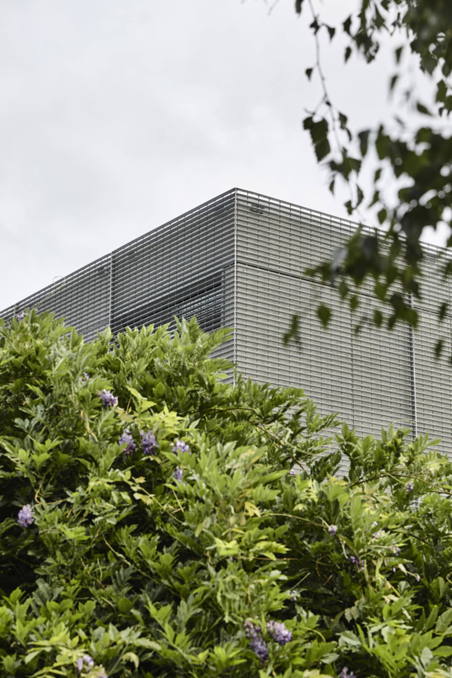 A modern building with a metallic frame and greenery in the foreground.