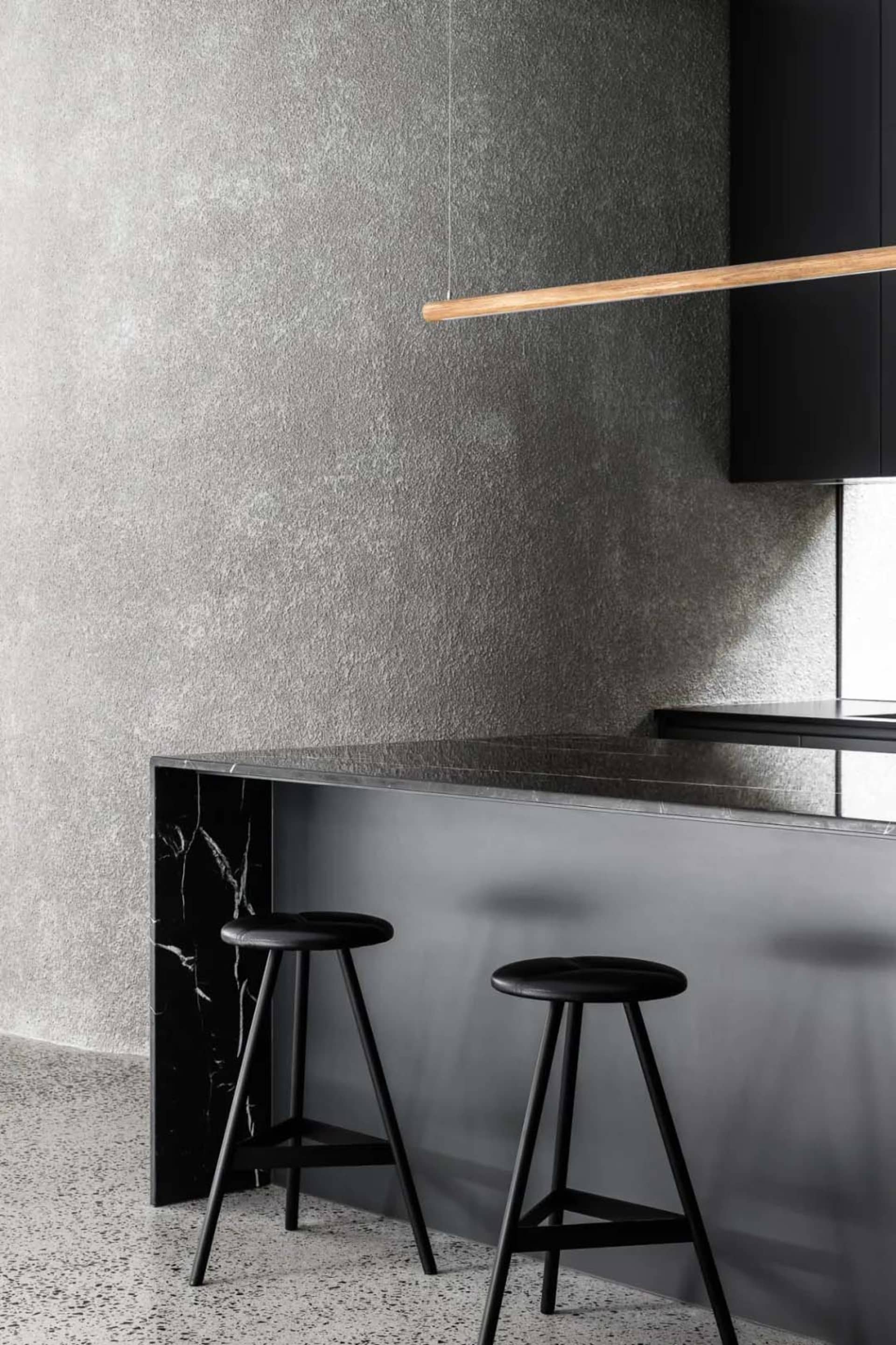 Modern kitchen counter with black and grey marble top and black stools.