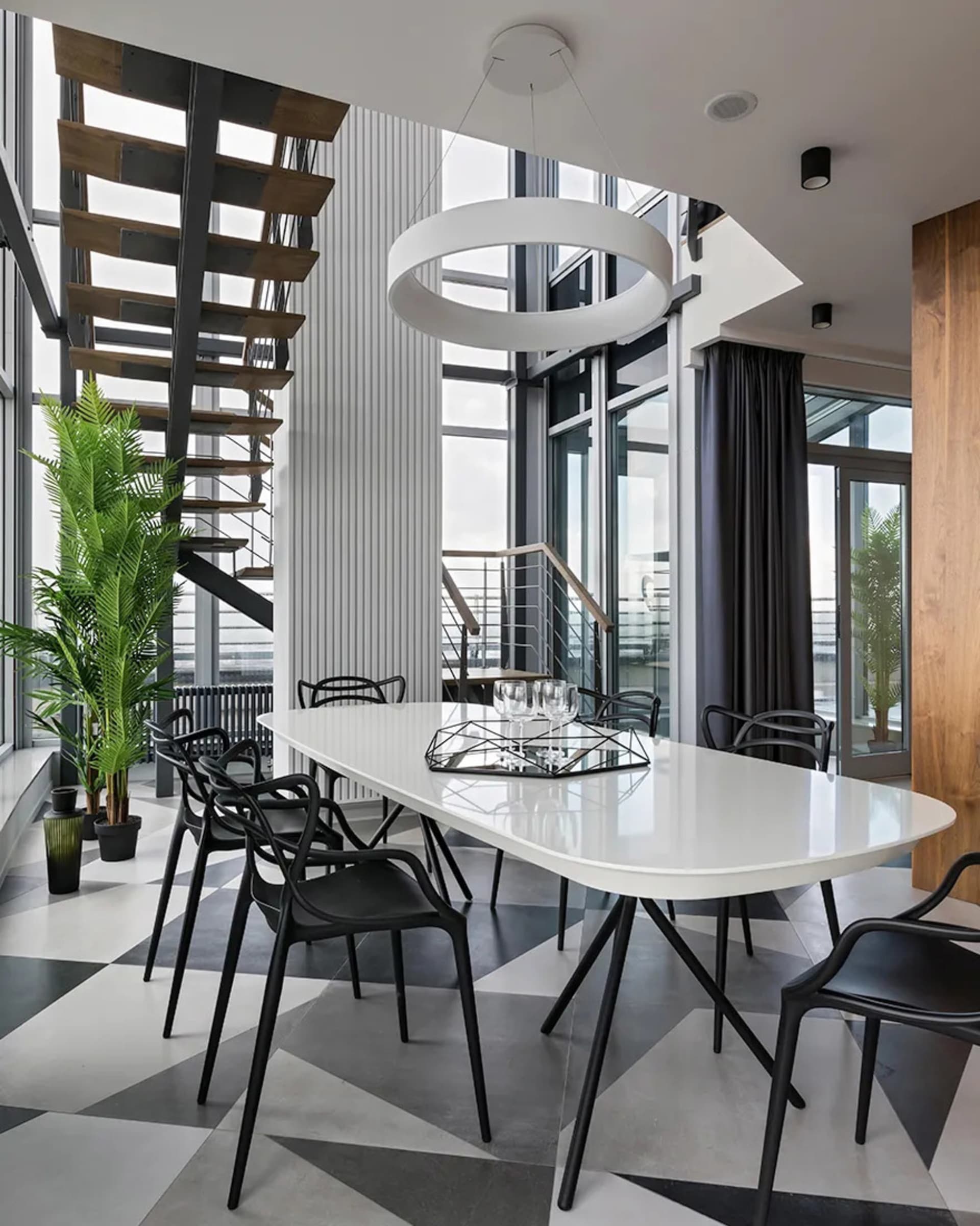 Modern dining room featuring a white oval table with black legs surrounded by black chairs on a geometric floor, illuminated