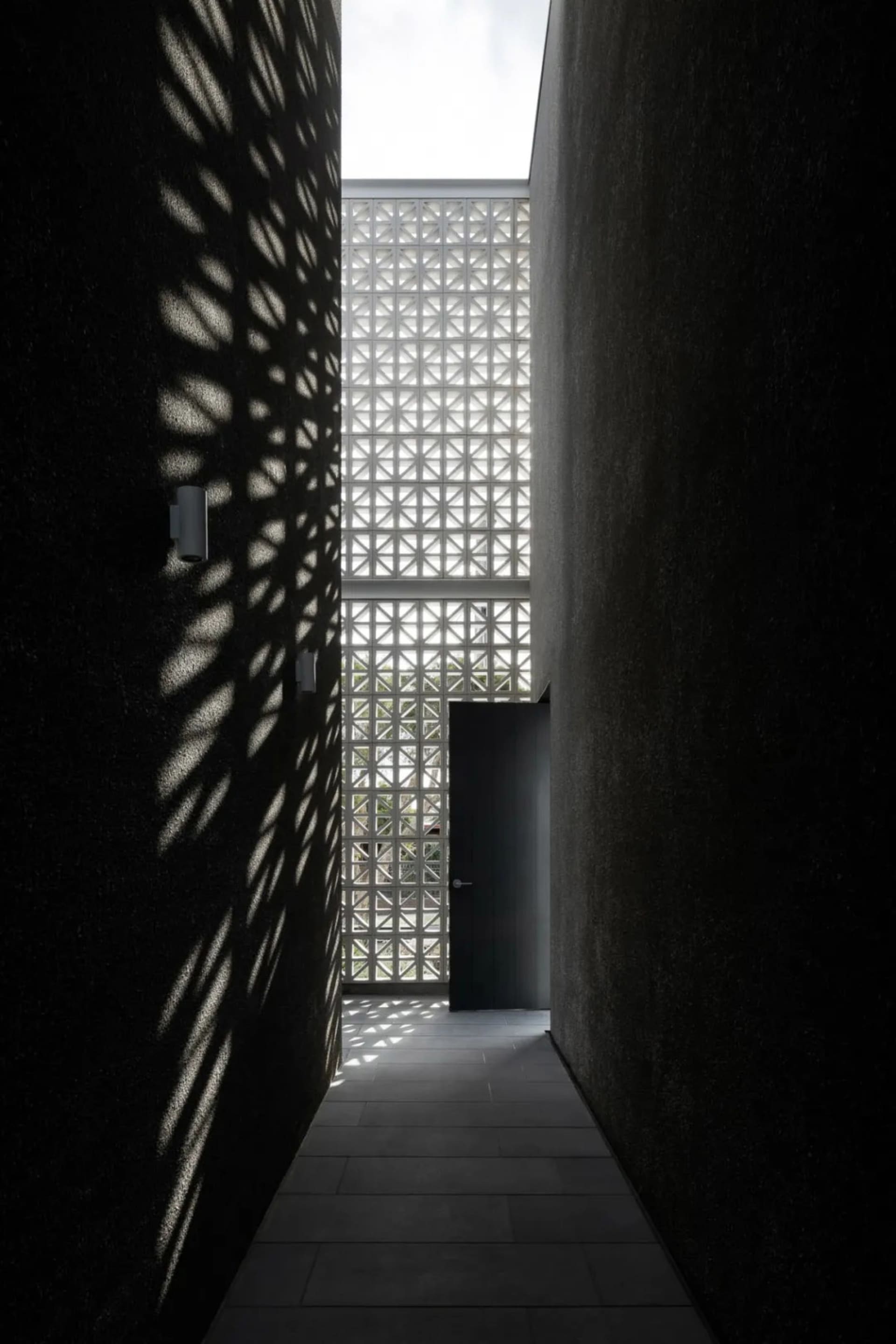 A corridor with concrete walls displaying geometric shadows created by a grid-like structure above.