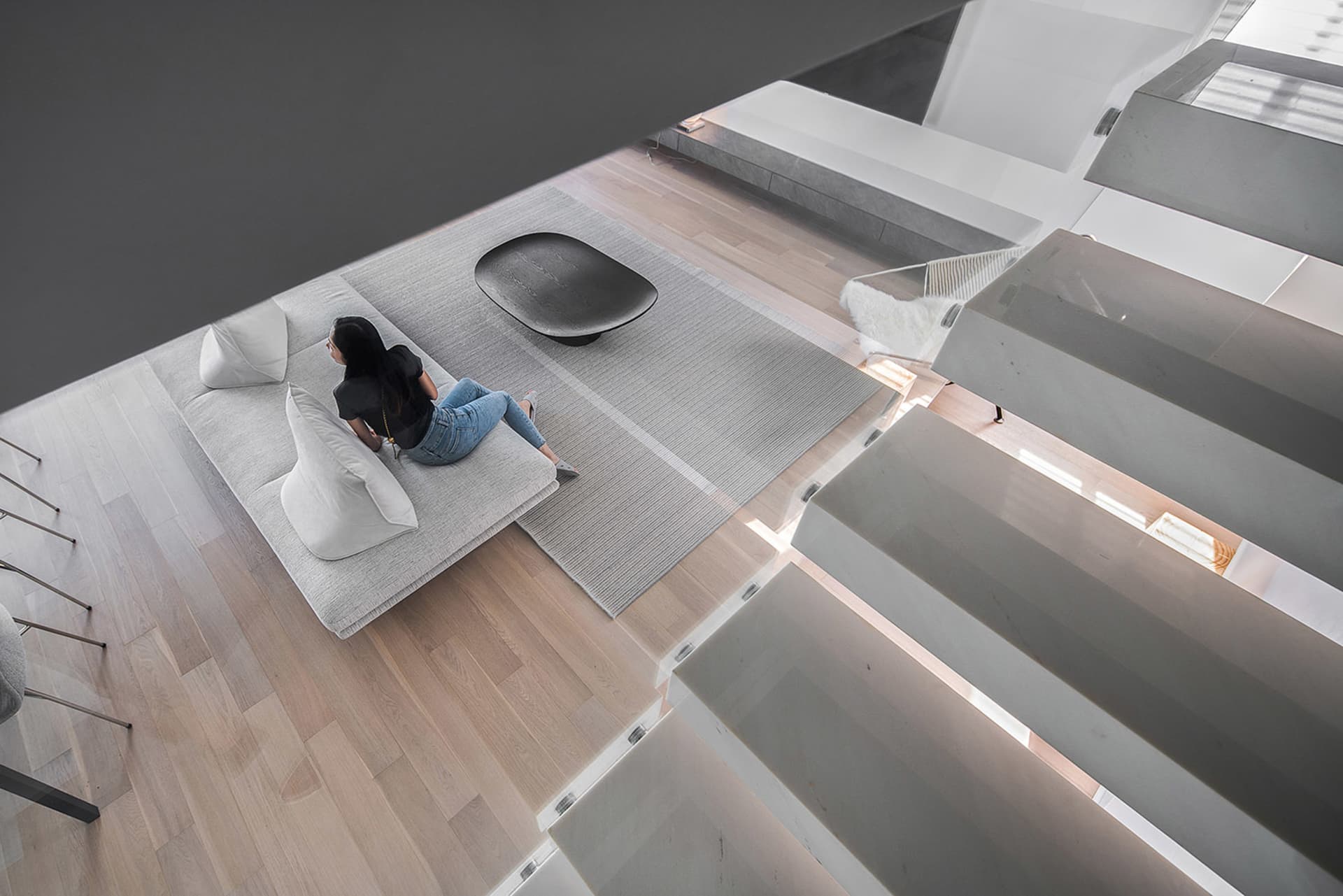A modern living room with a gray cushioned sofa, wooden flooring, and a black decorative bowl on a rug.