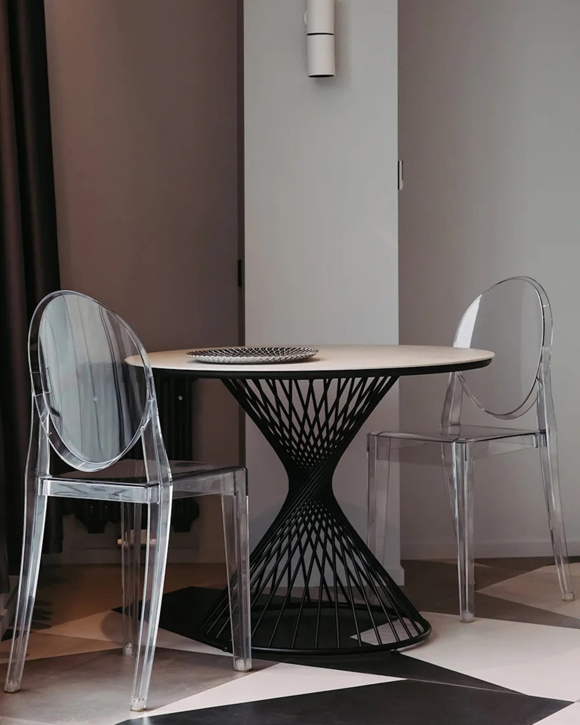 A modern dining area with a round table, two transparent chairs, and a decorative plate on the table.