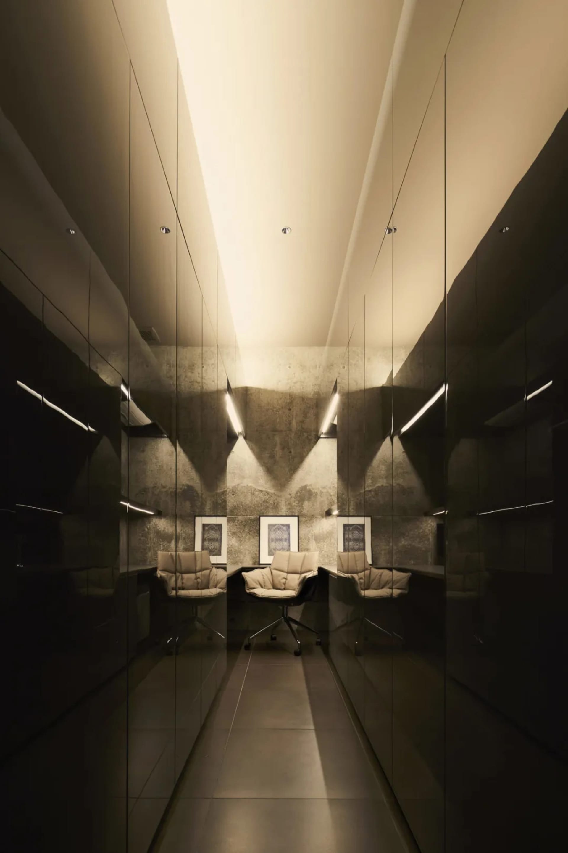 An image of a modern minimalist office with concrete walls, illuminated by warm lighting and featuring functional furniture.