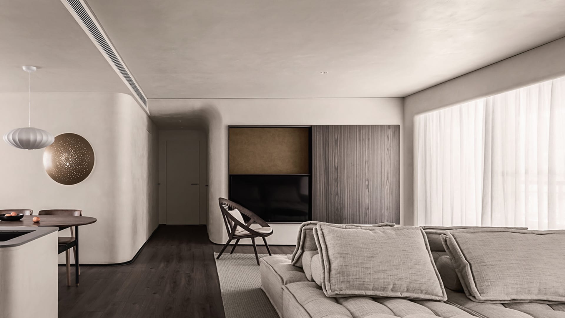 A minimalist living room with a large sectional sofa, a wooden armchair, and a dining area with a round table and chairs.