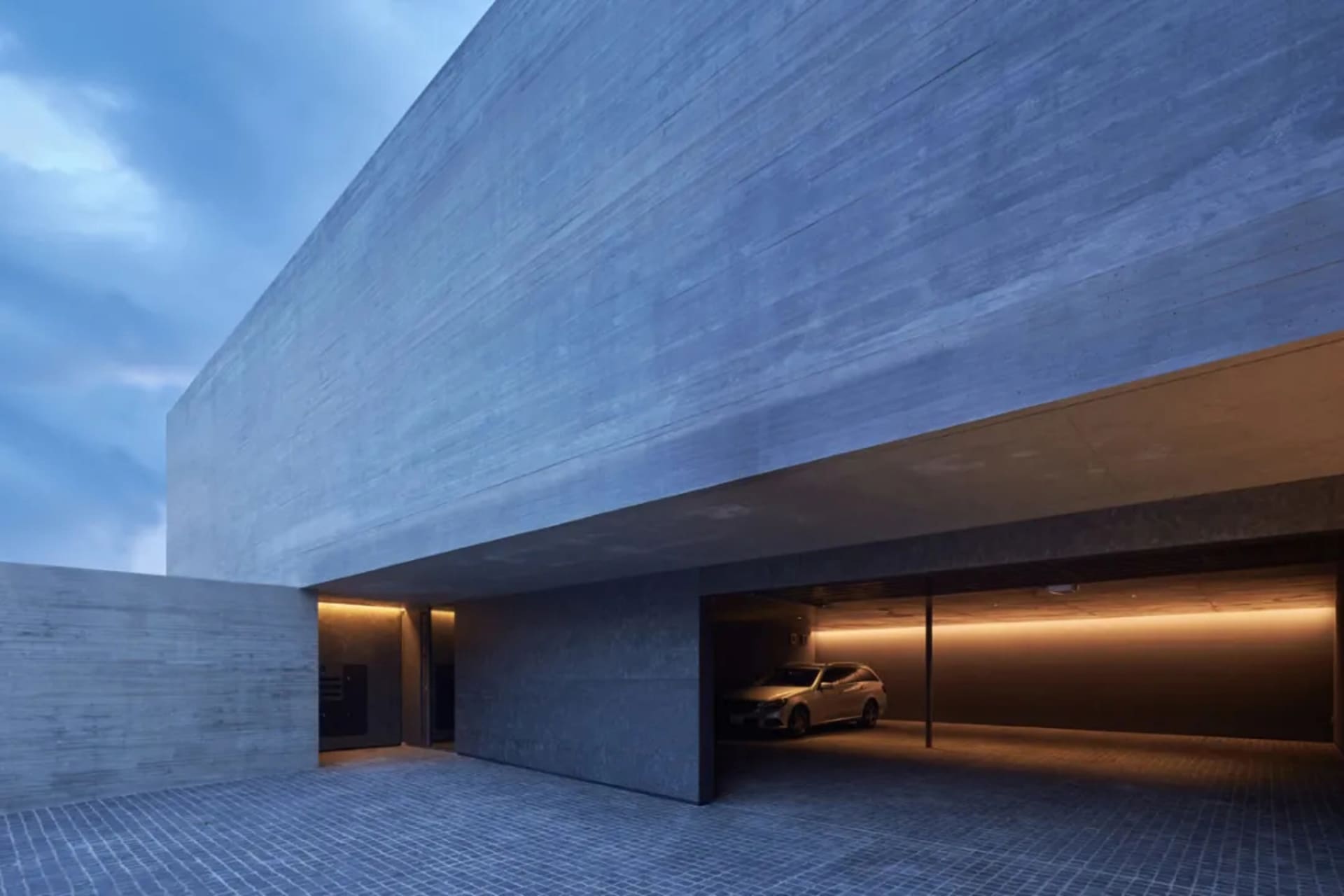 A modern garage constructed of concrete with a single car parked inside.