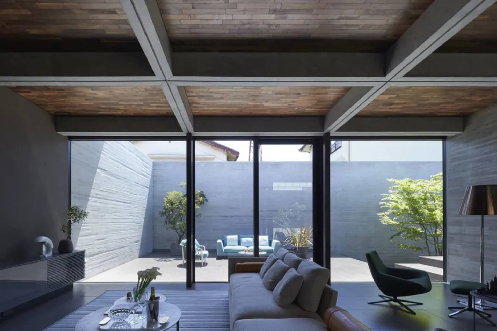 A modern concrete living room featuring a cozy sofa, stylish furniture, and large windows overlooking a serene courtyard.