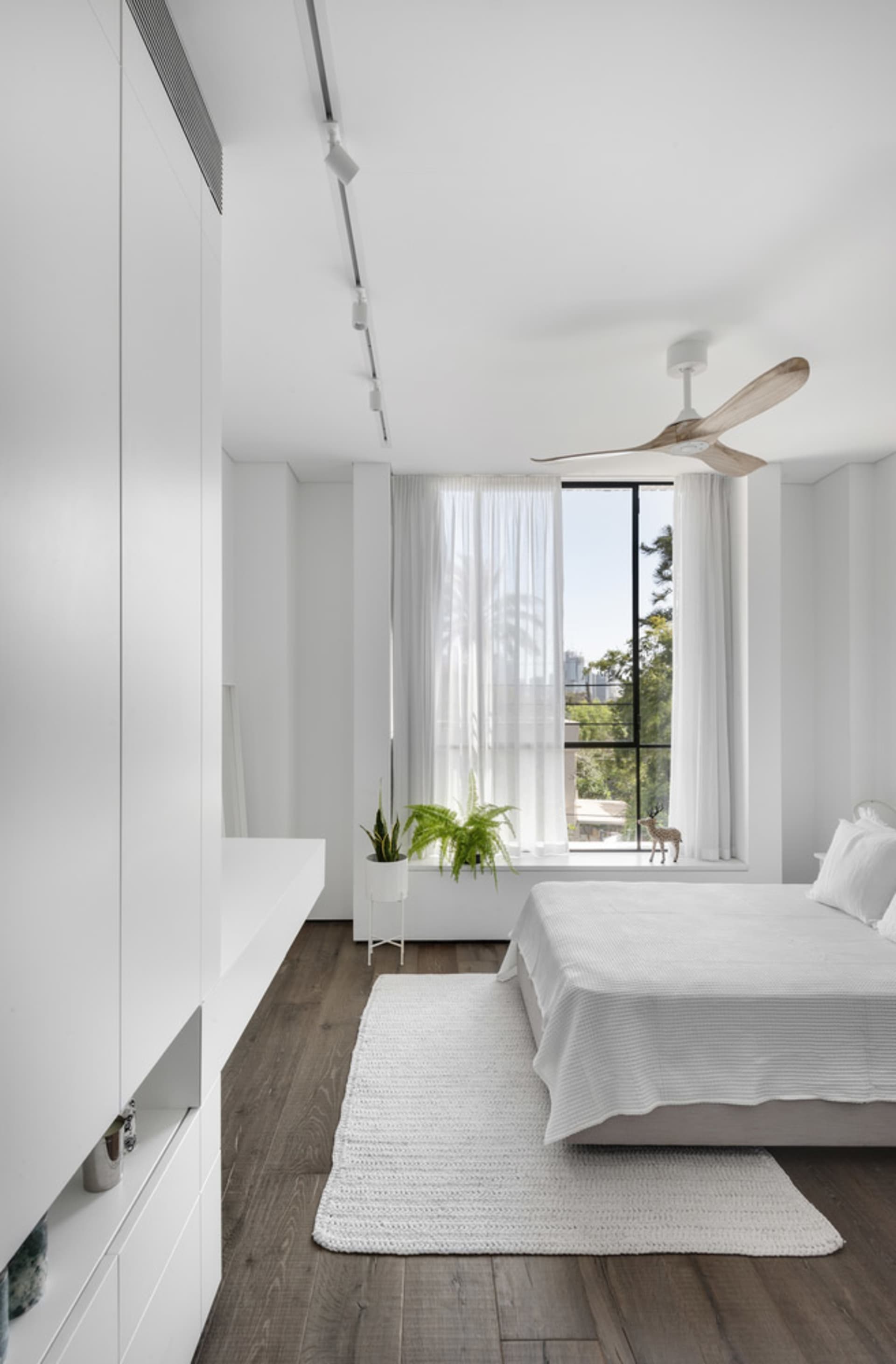 A modern minimalist bedroom featuring white furniture and a wooden floor.