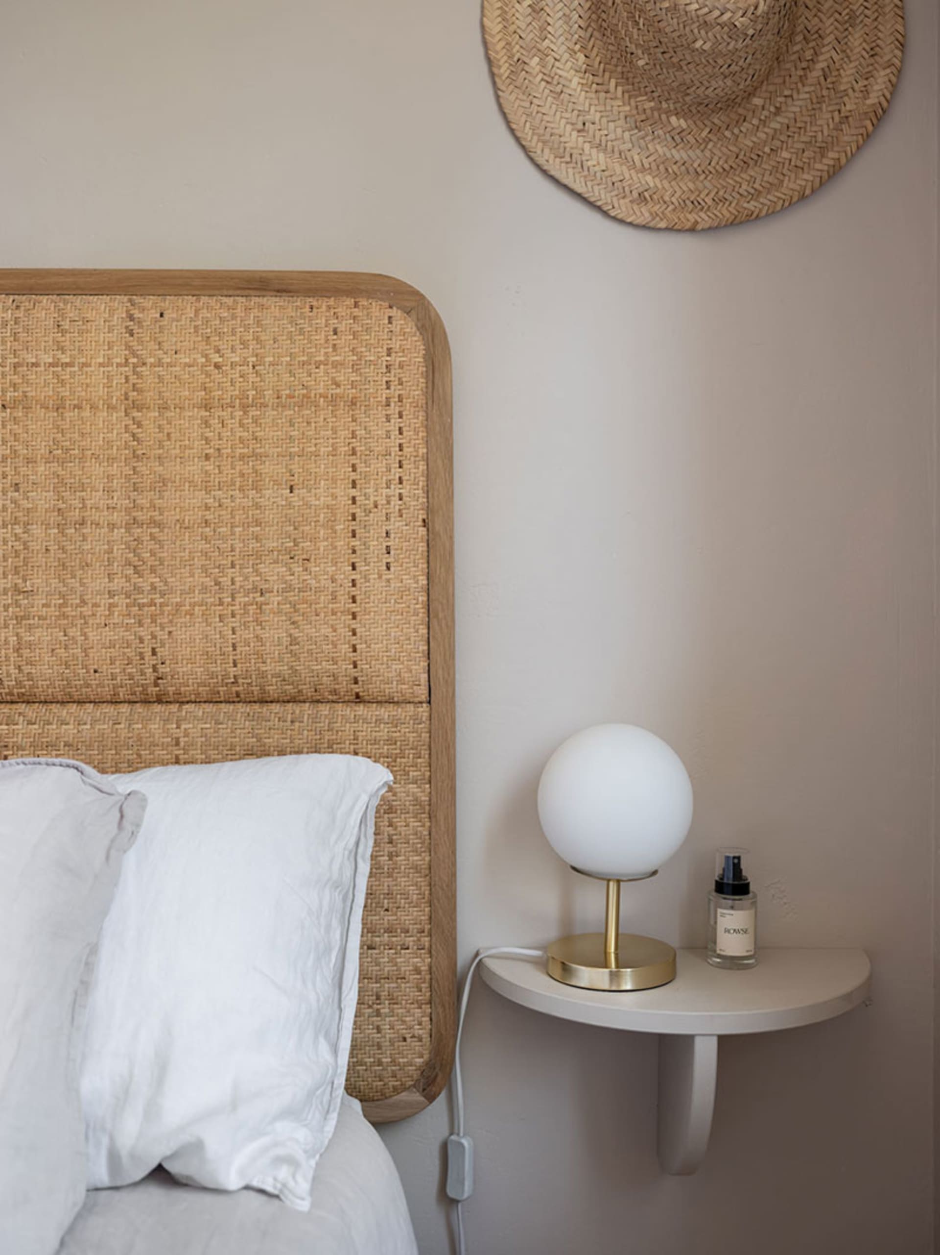 Minimalist bedroom with a woven bed frame and a wall-mounted nightstand with a spherical light and essential oil spray.