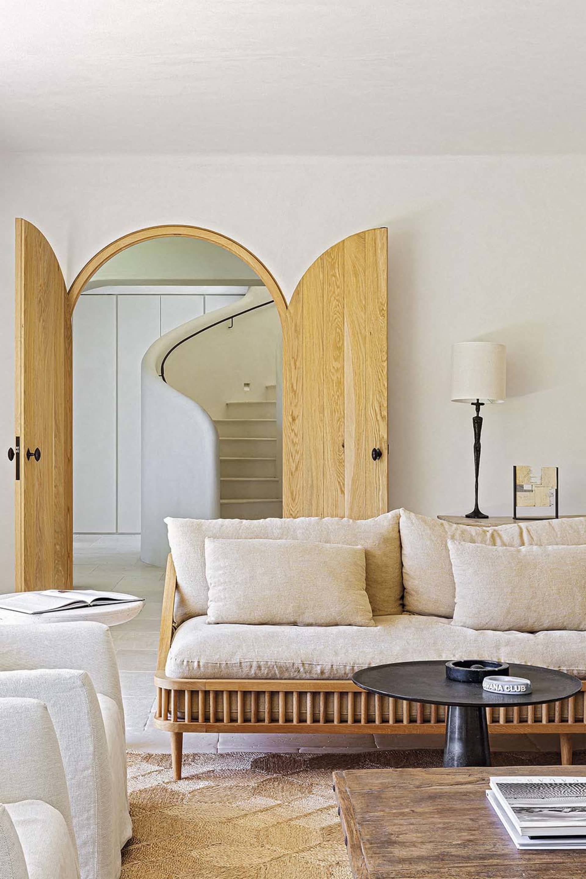 Minimalist-style living room with a wooden sofa, wooden coffee table, and white accent chairs, featuring a wooden-framed door