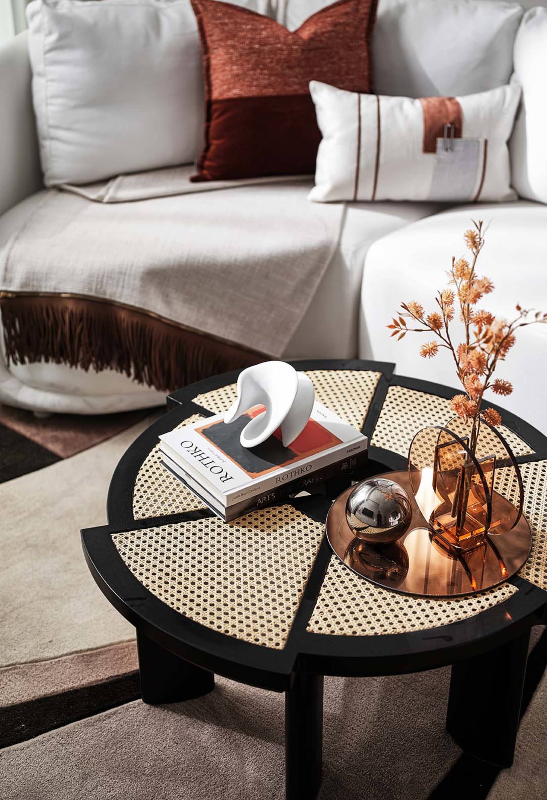 A modern living room featuring a coffee table with a geometric black frame and rattan top, adorned with decorative objects an
