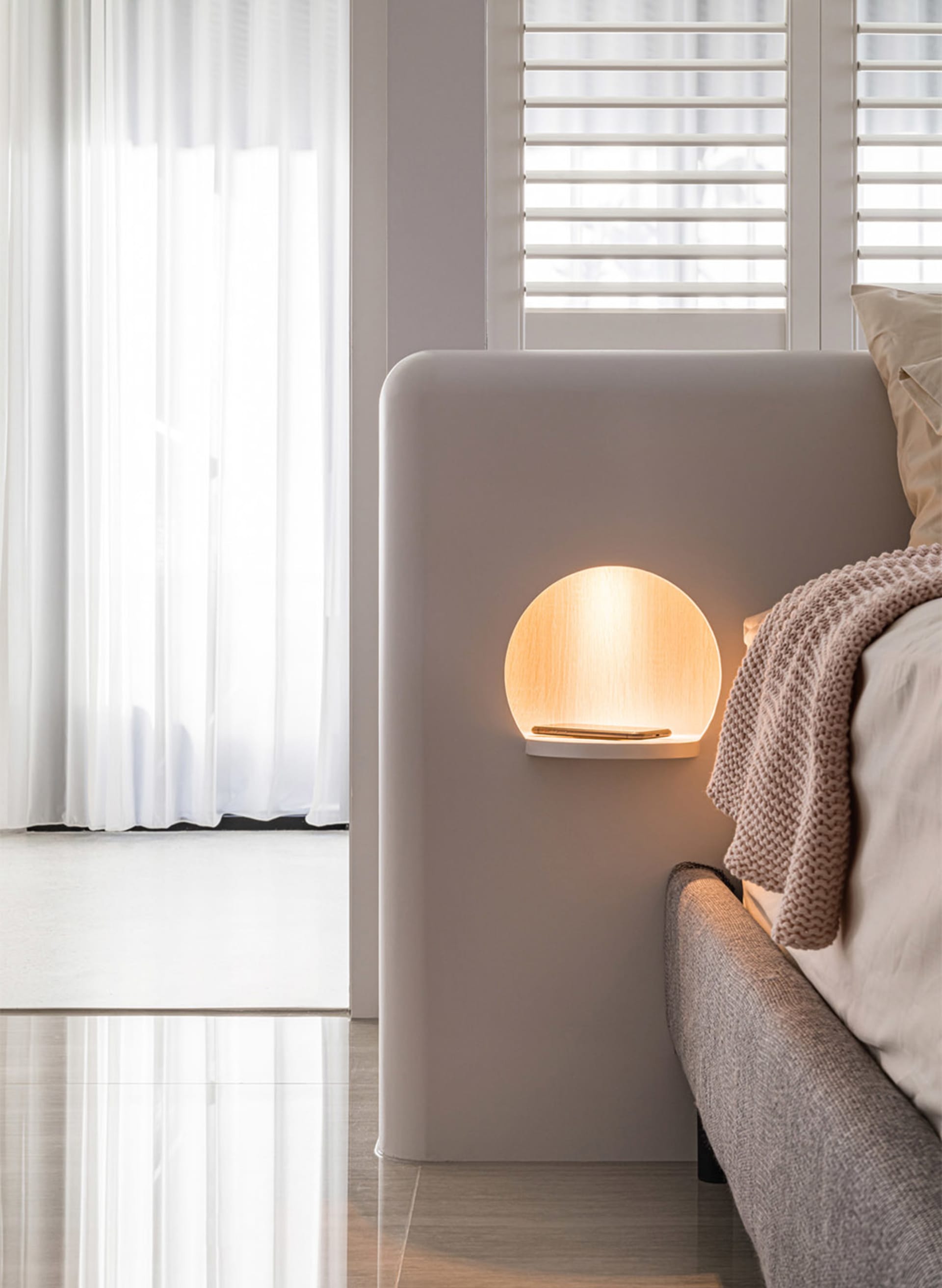 A minimalist bedroom with a soft, ambient light from a circular wall lamp made of light-colored wood.