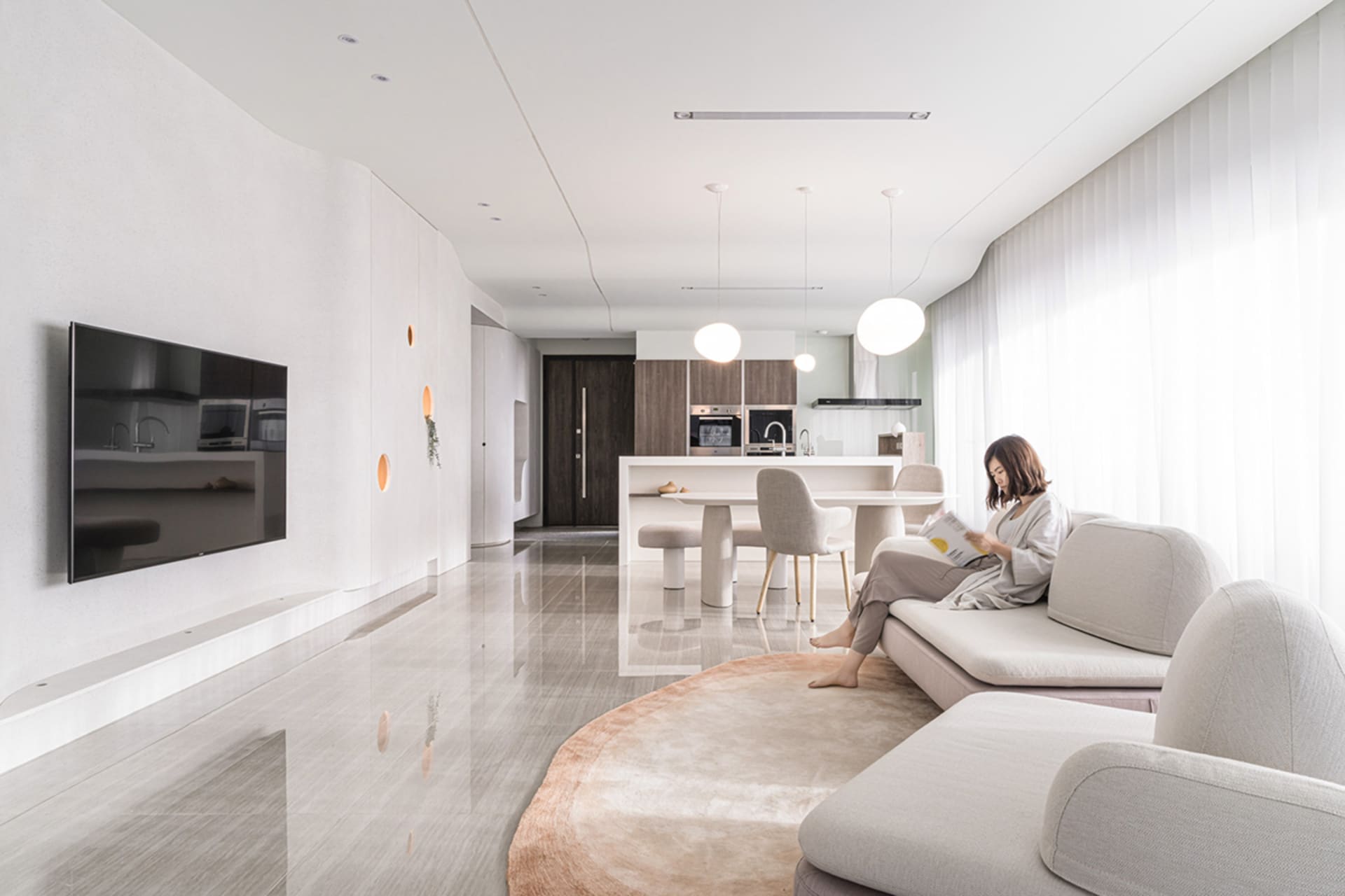 A modern interior living space with neutral tones, featuring a large sofa, a coffee table, a TV, and a dining area in the bac