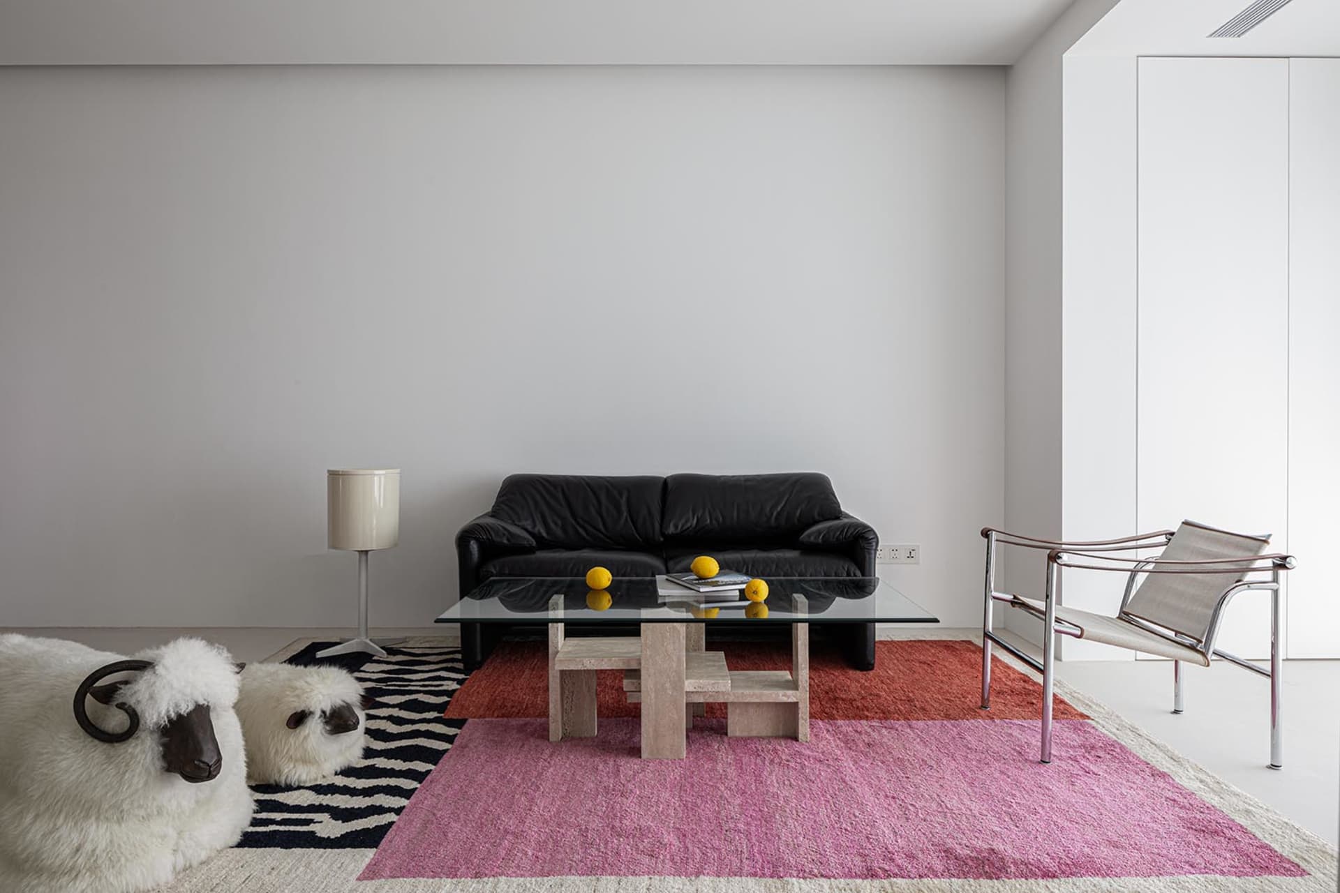 Interior view of a modern living room with a black leather sofa, glass coffee table, and colorful rugs. Modern, minimalist de
