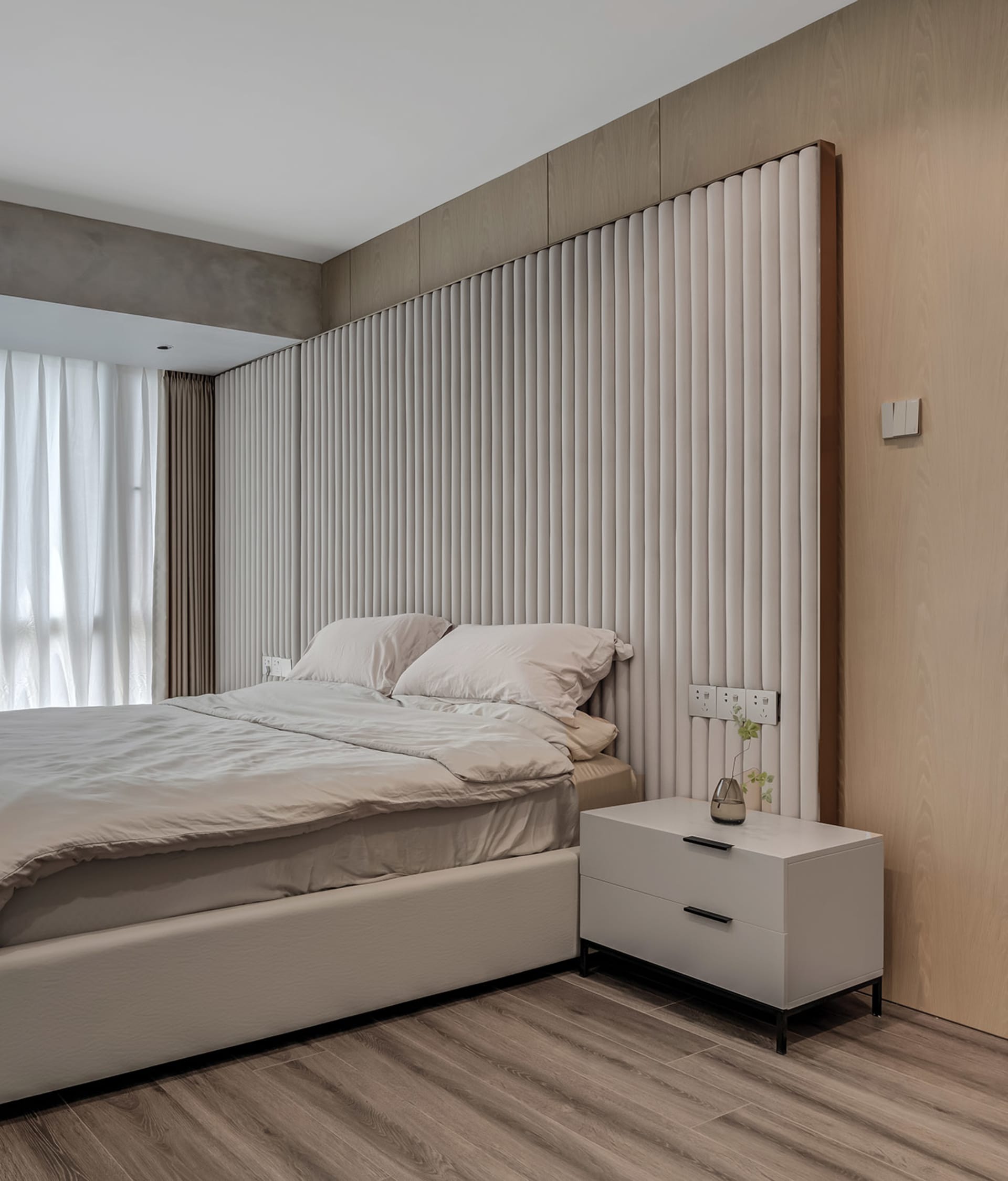 A minimalist bedroom with a textured fabric headboard and beige bedding.