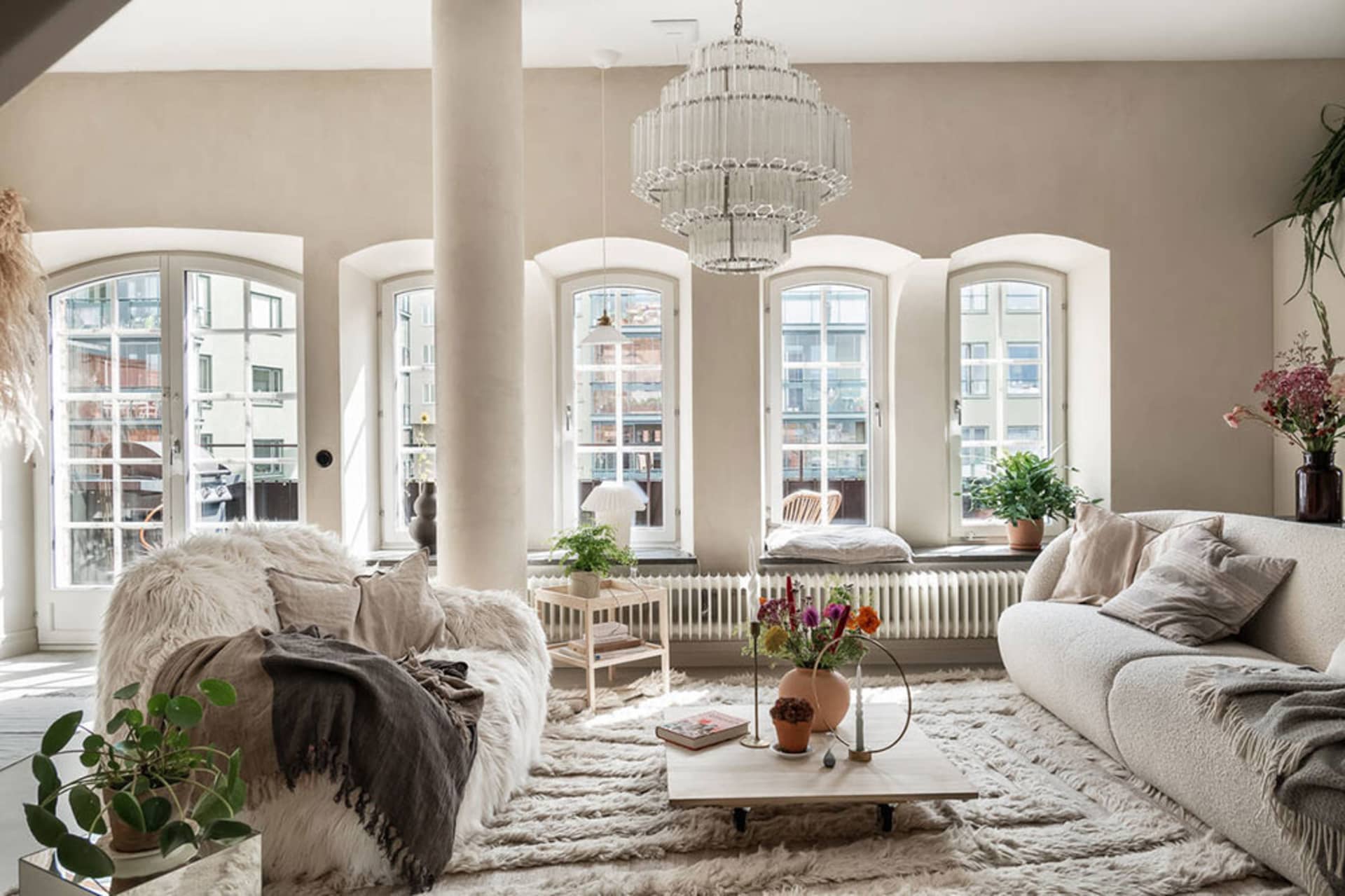 A minimalist living room with a neutral color palette, natural materials, and ample sunlight from large arched windows.