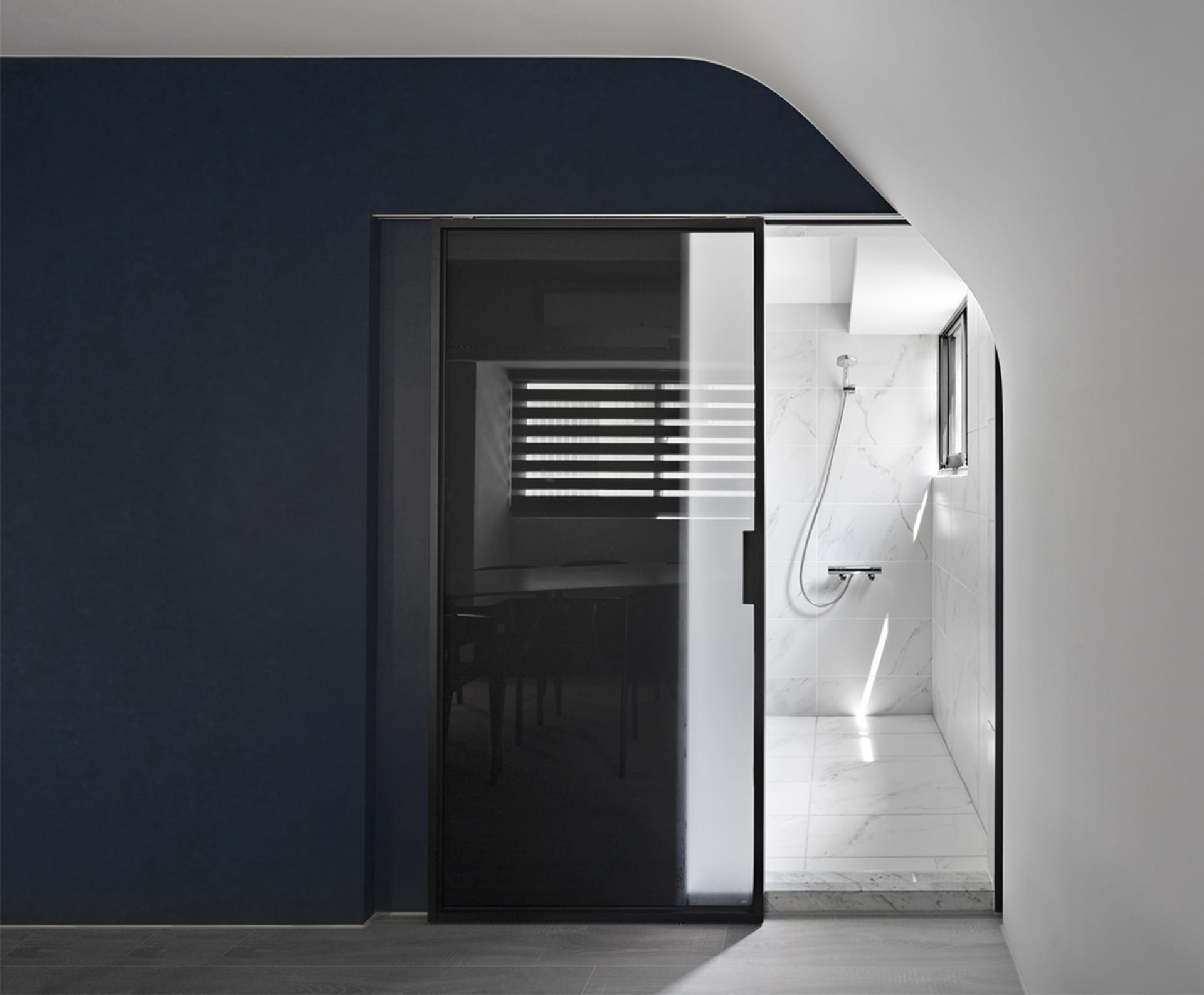 Minimalist modern bathroom with marble walls, glass shower enclosure, and wooden floor.