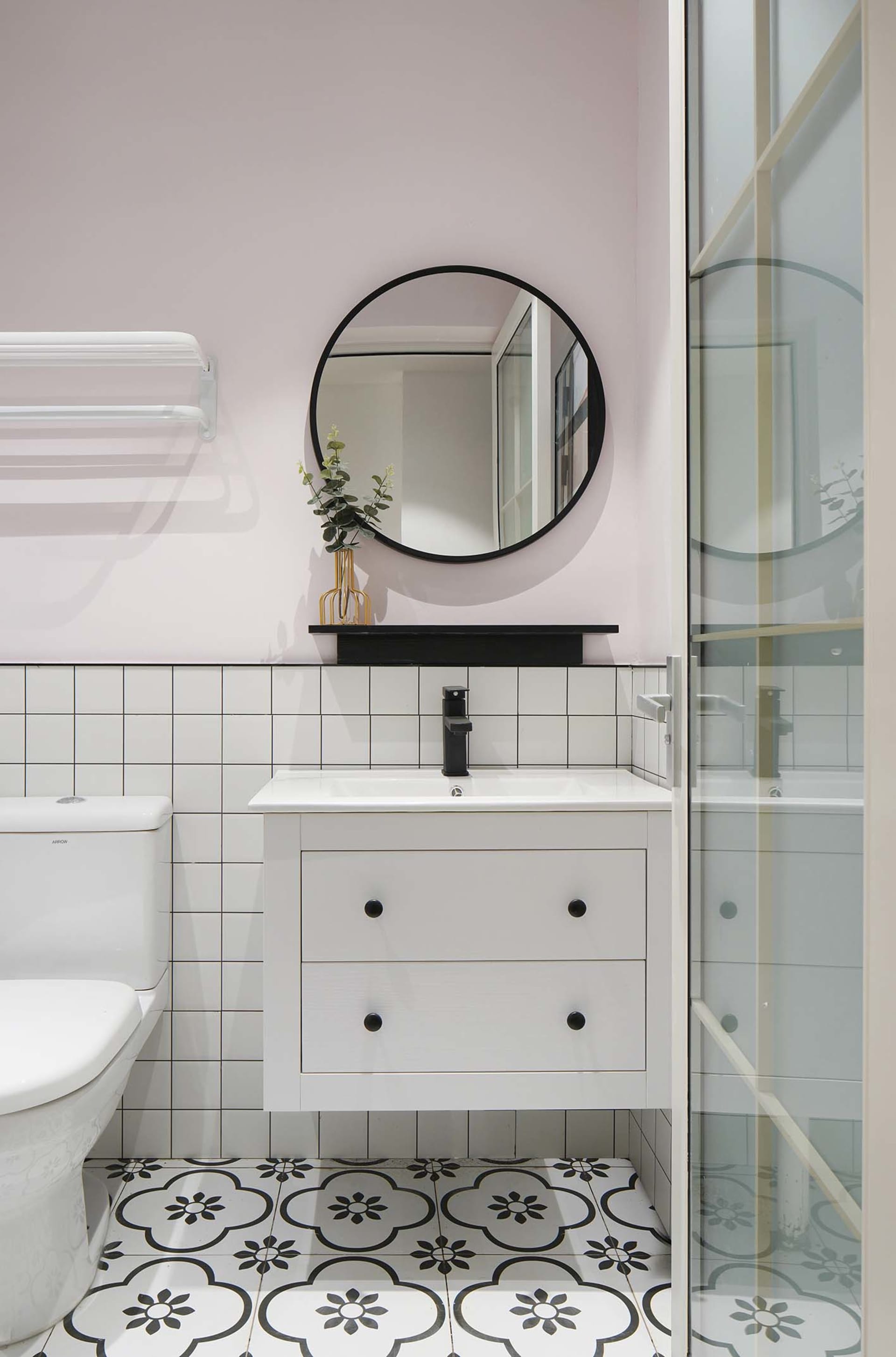 Modern bathroom with white tiled walls and a cement floor, featuring a vanity sink, toilet, and glass shower door.