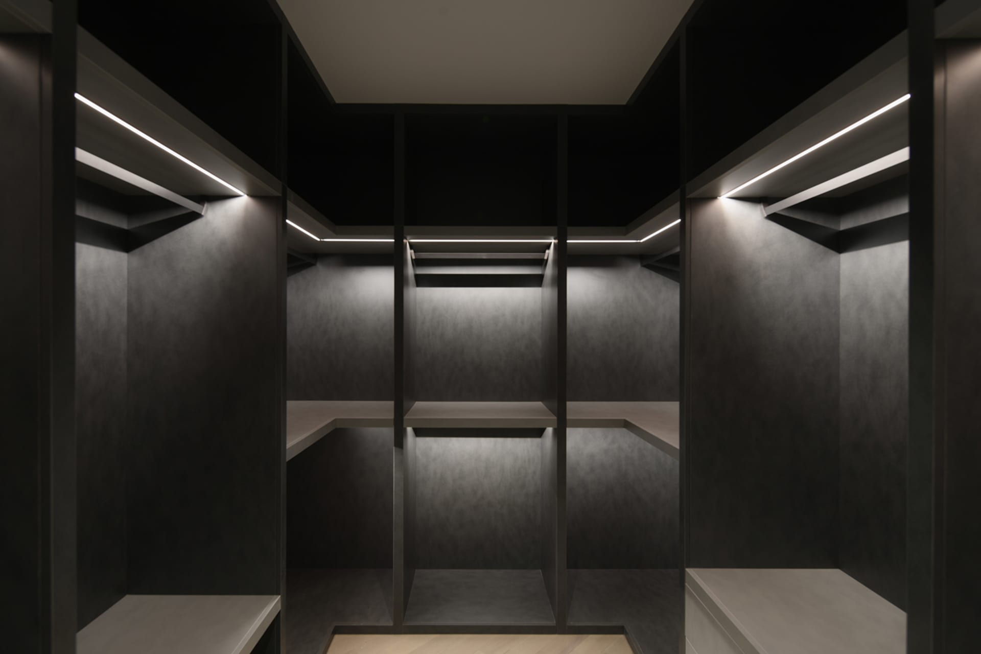 An empty, minimalist closet with concrete walls and shelves illuminated by embedded lighting.