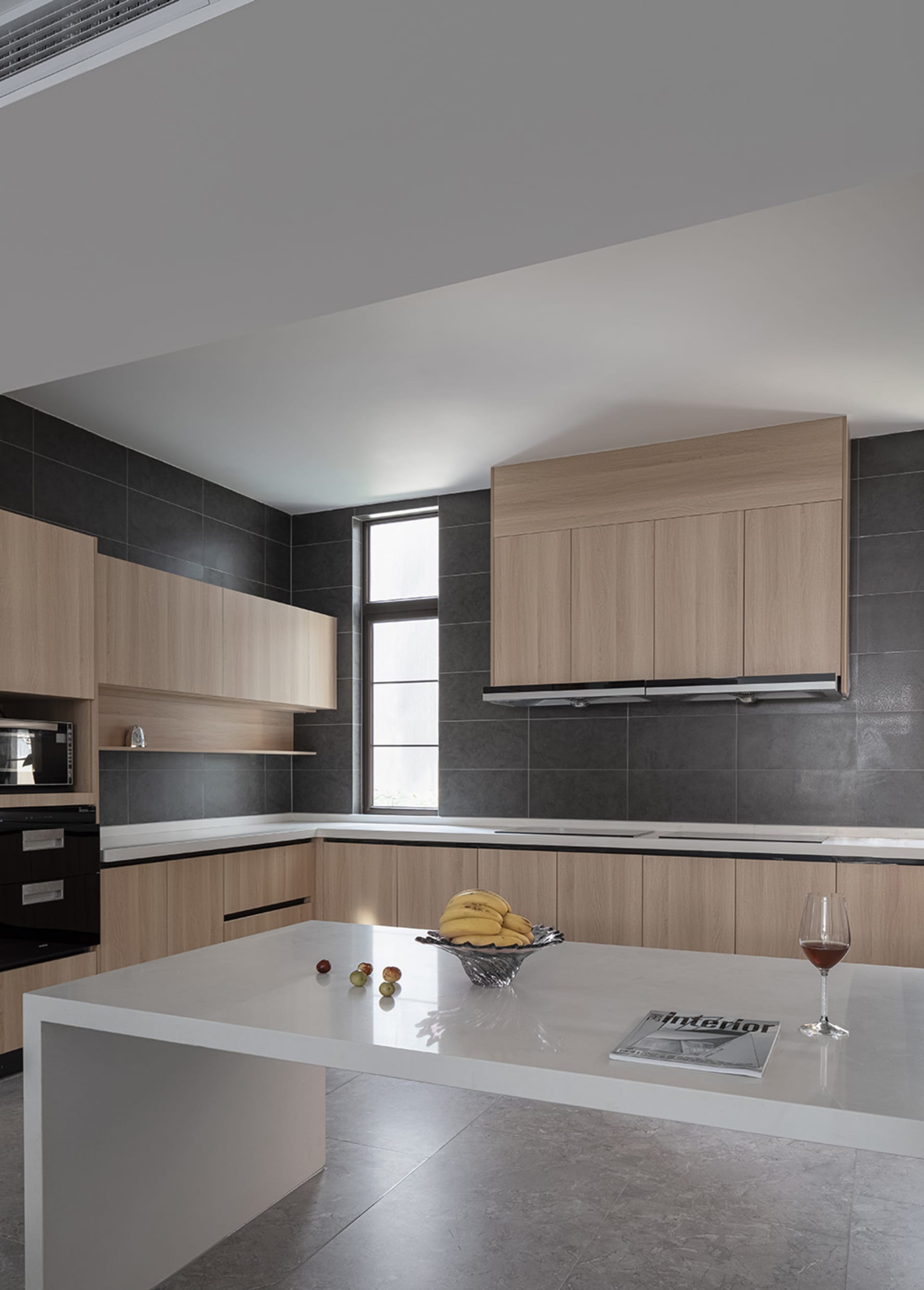 A modern minimalist residential kitchen with black tiles, wooden cabinets, and a white countertop.