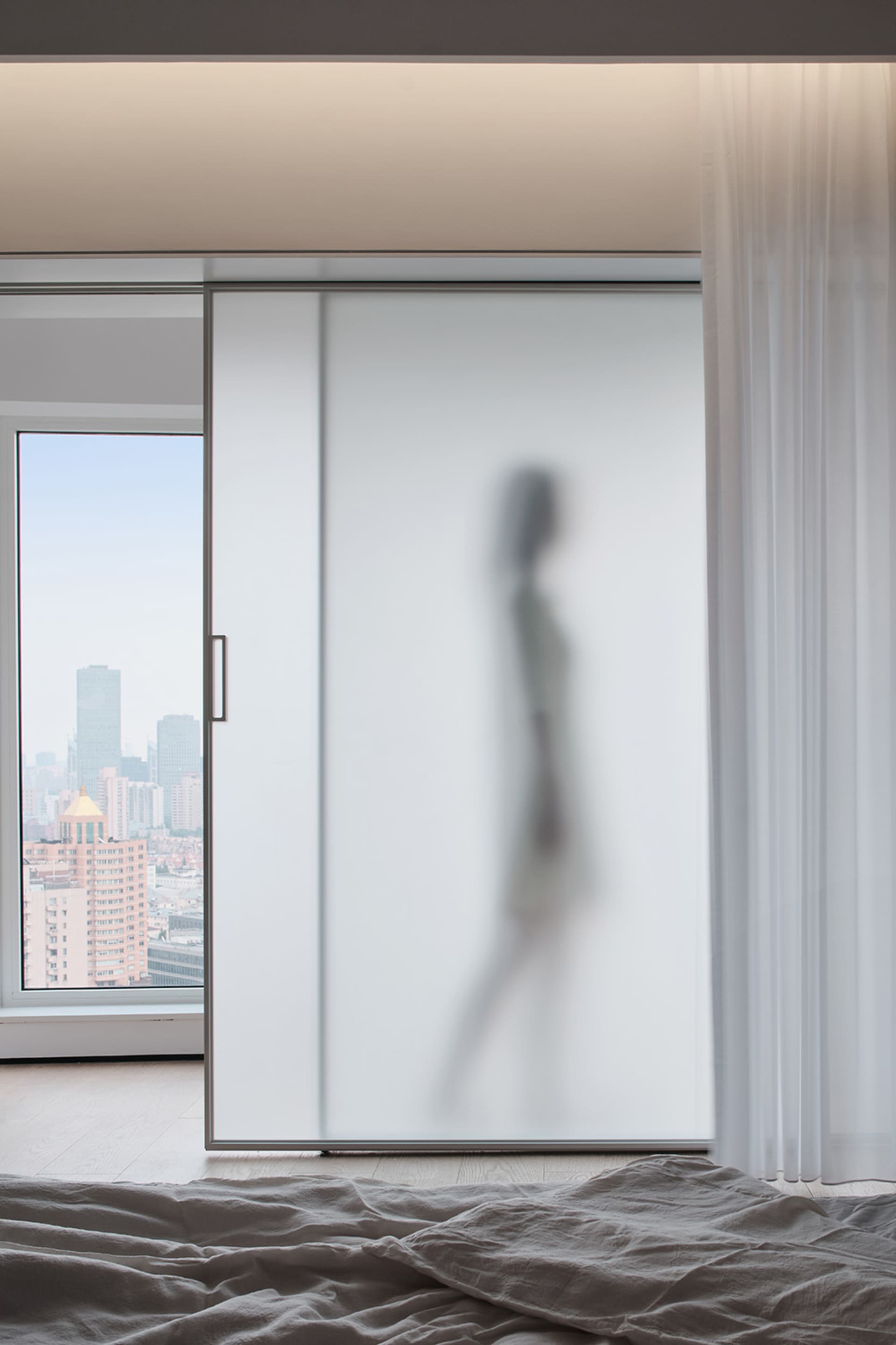 A modern minimalist residential space featuring glass walls and a view of the cityscape.