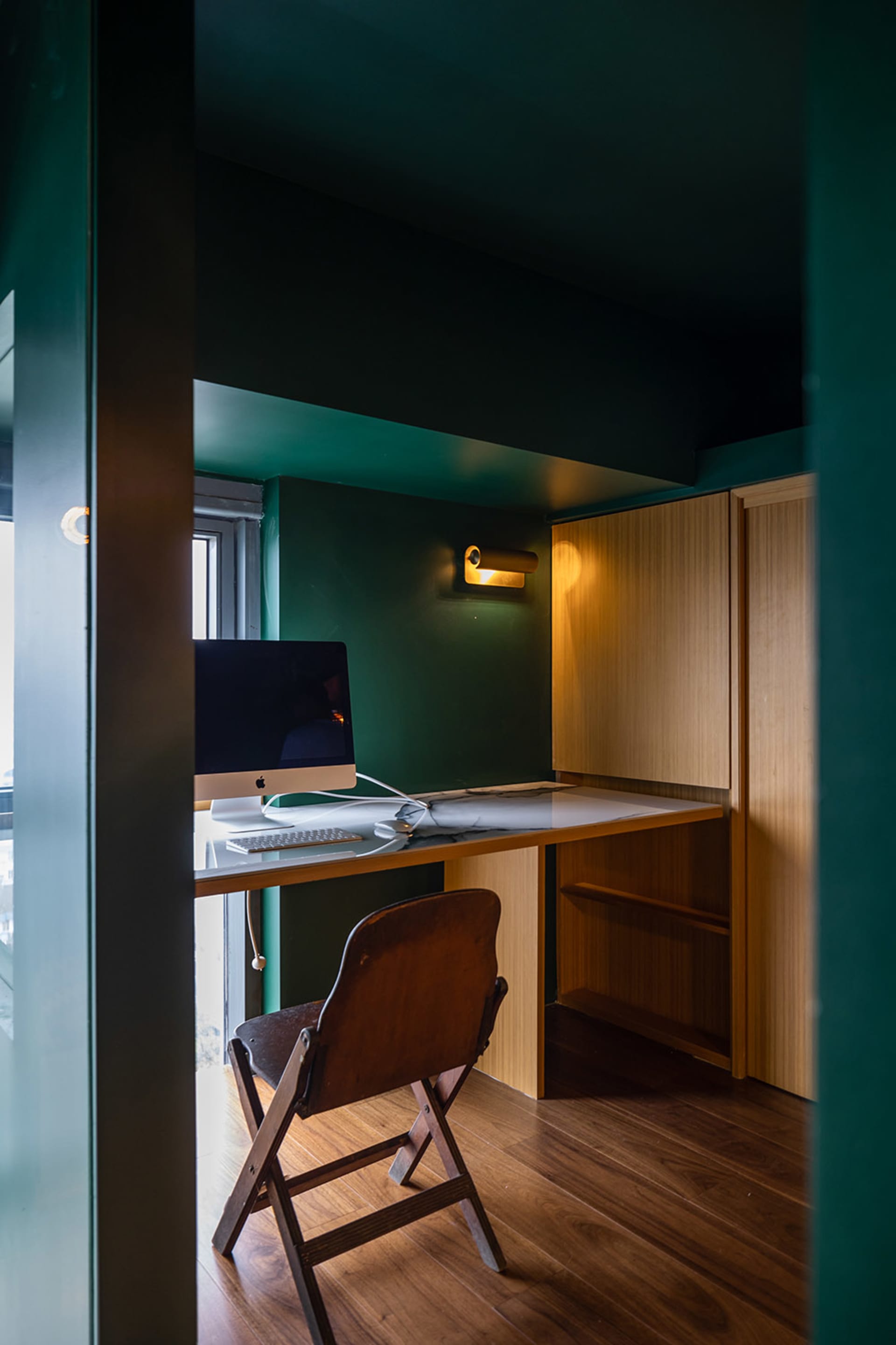 A minimalist home office featuring a wooden desk with a computer setup, a chair, and a shelf.