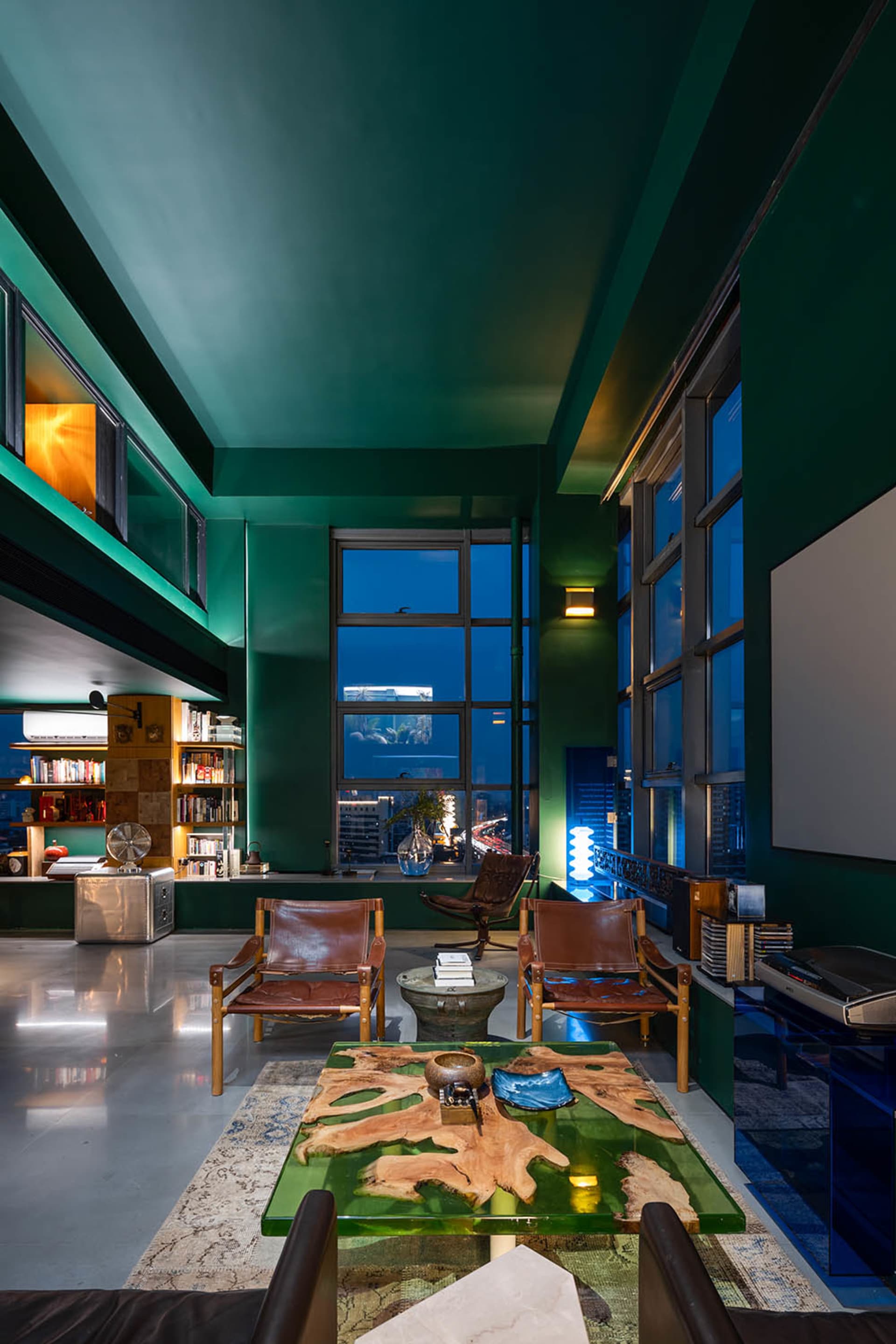 A modern industrial living room featuring glass walls, leather chairs, metallic accents, and wooden elements.