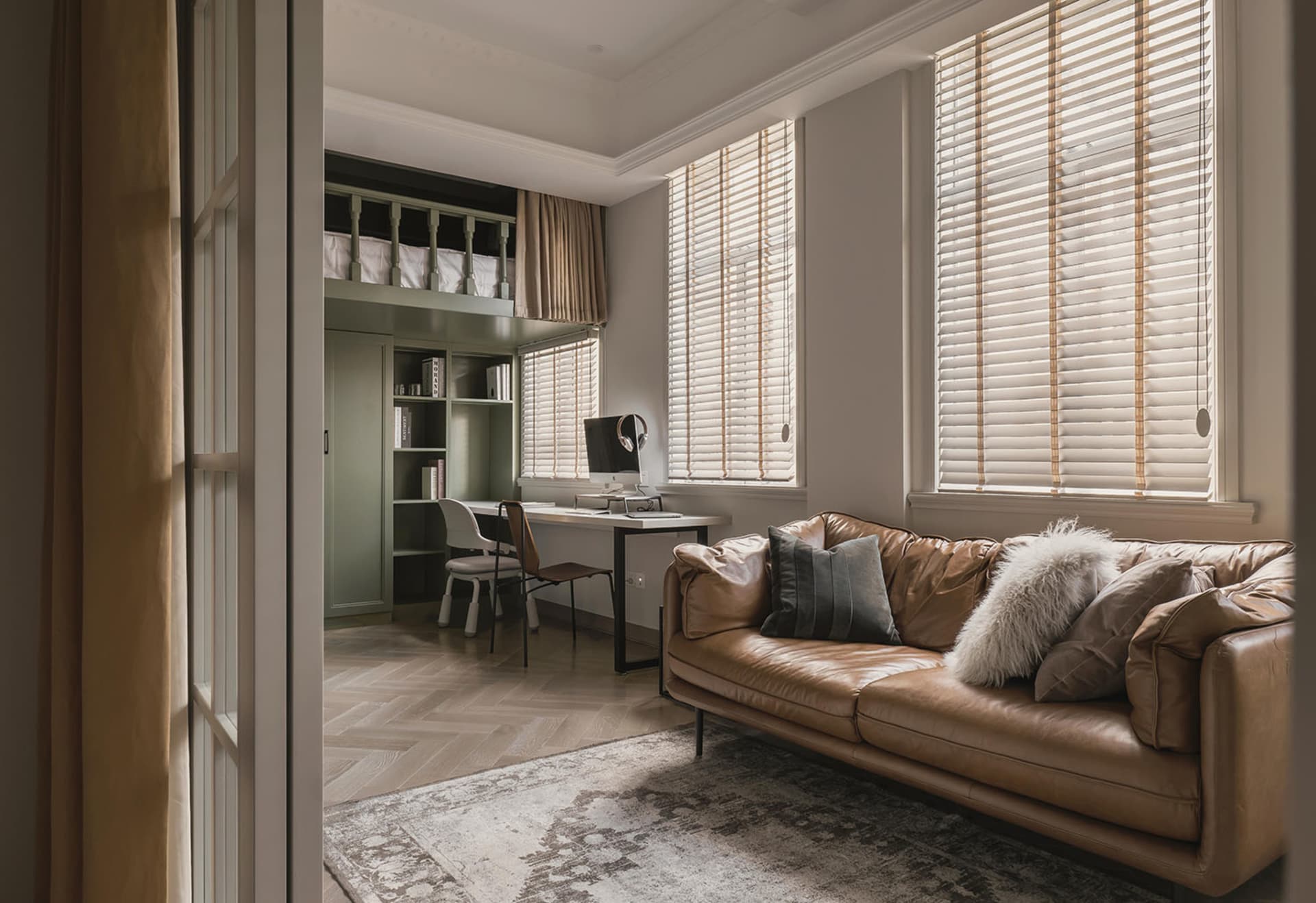 Modern living room office with wooden furniture, leather couch, and blinds on windows.