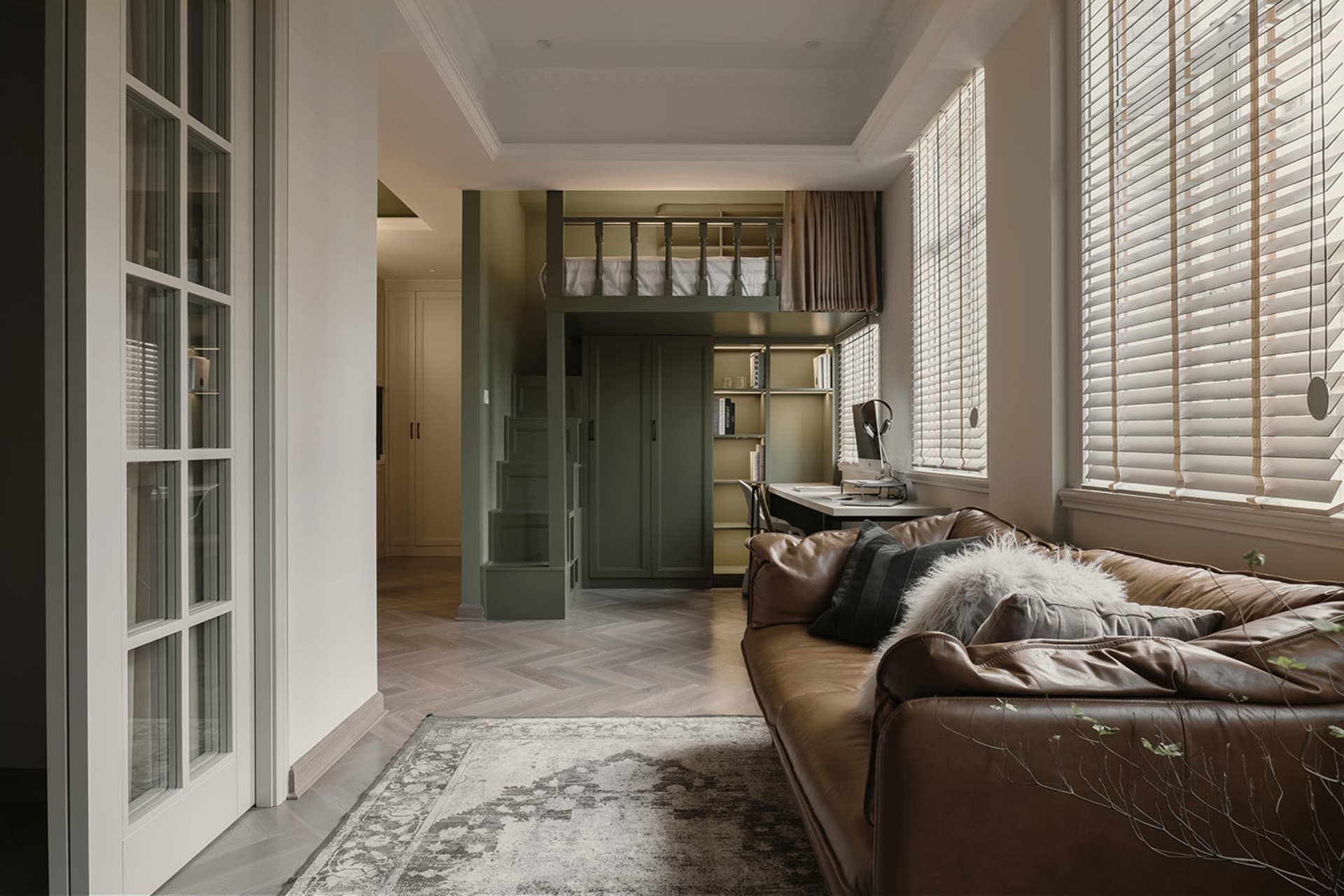 A modern living room featuring a brown leather couch, a rug, and a window with blinds.