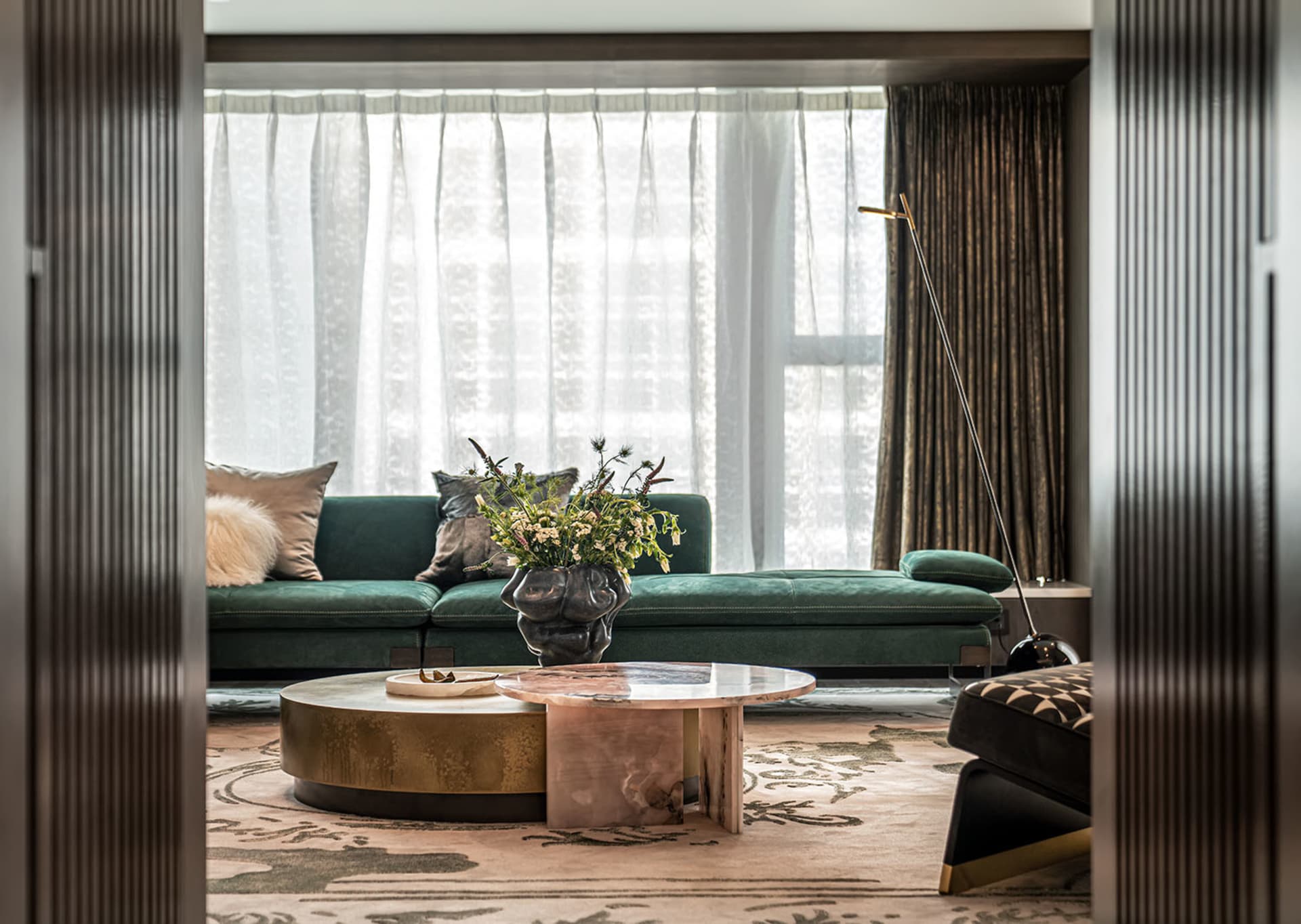 A modern living room featuring a green velvet sofa, marble coffee table, and brass accents.