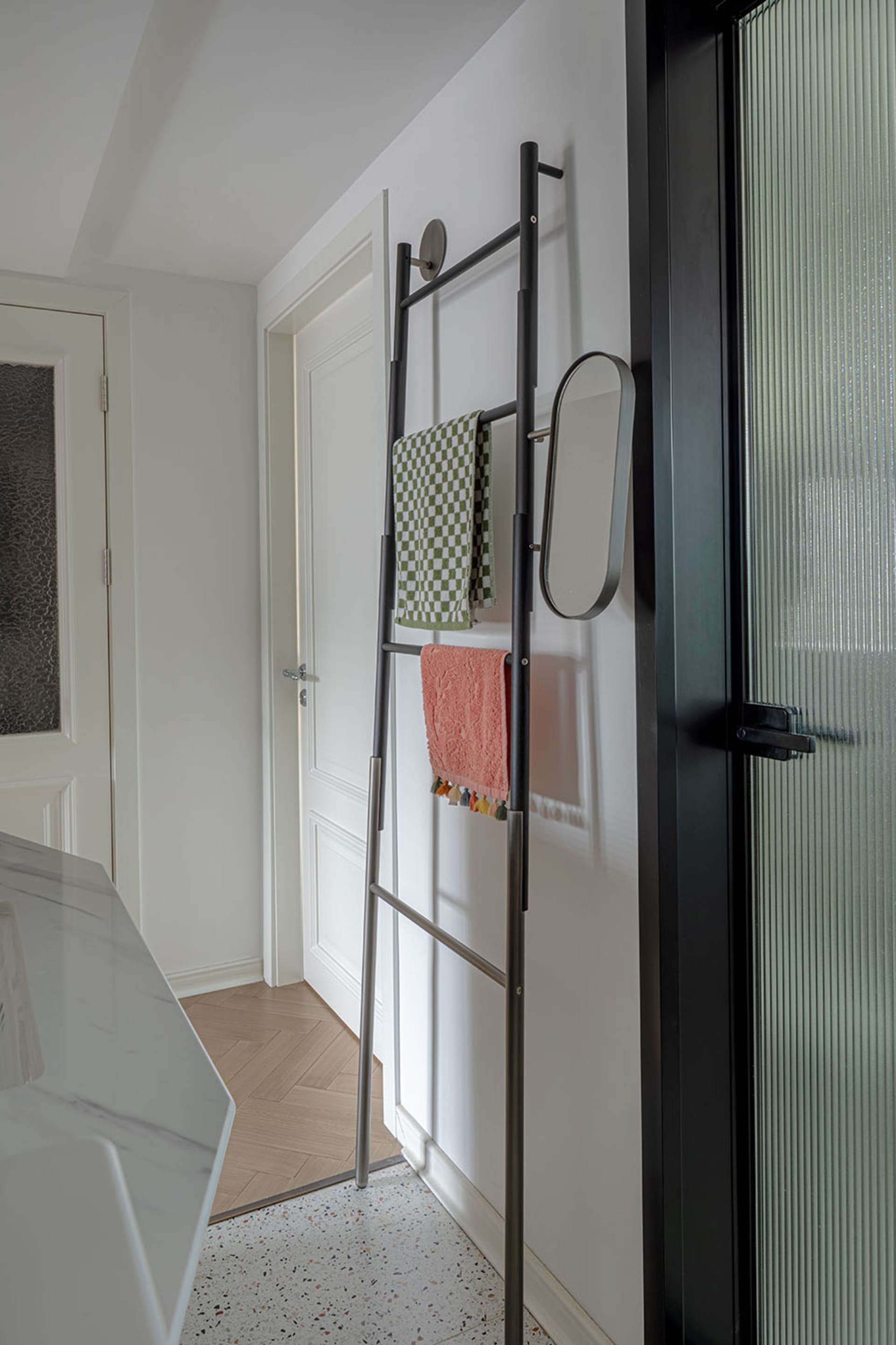 A minimalist bathroom with a modern metal towel rack holding checkered and pink towels.