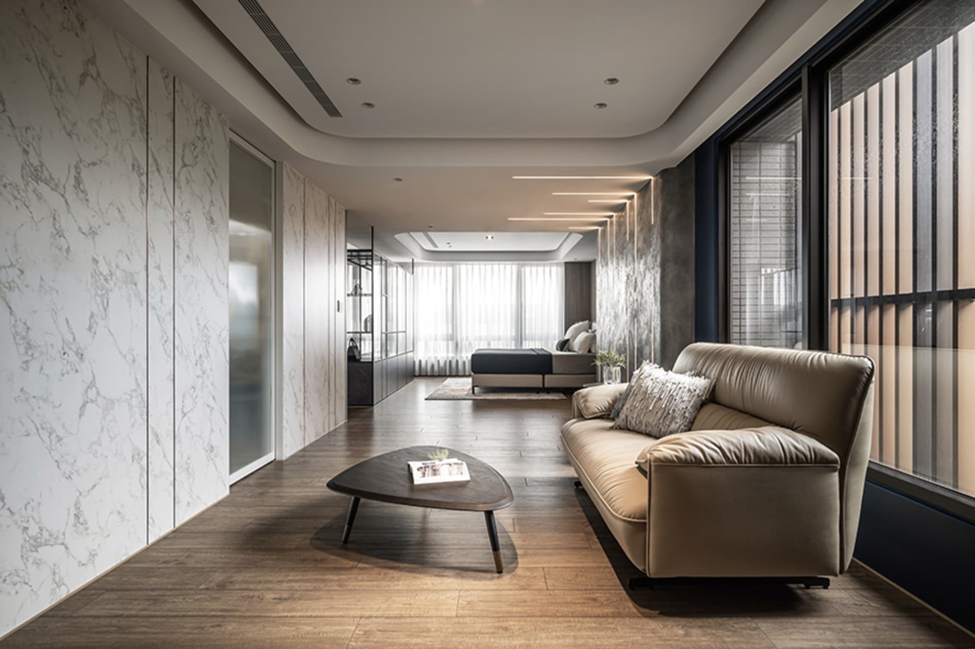 Modern living room featuring a white marble wall and floor, with a beige leather sofa and a contemporary coffee table.