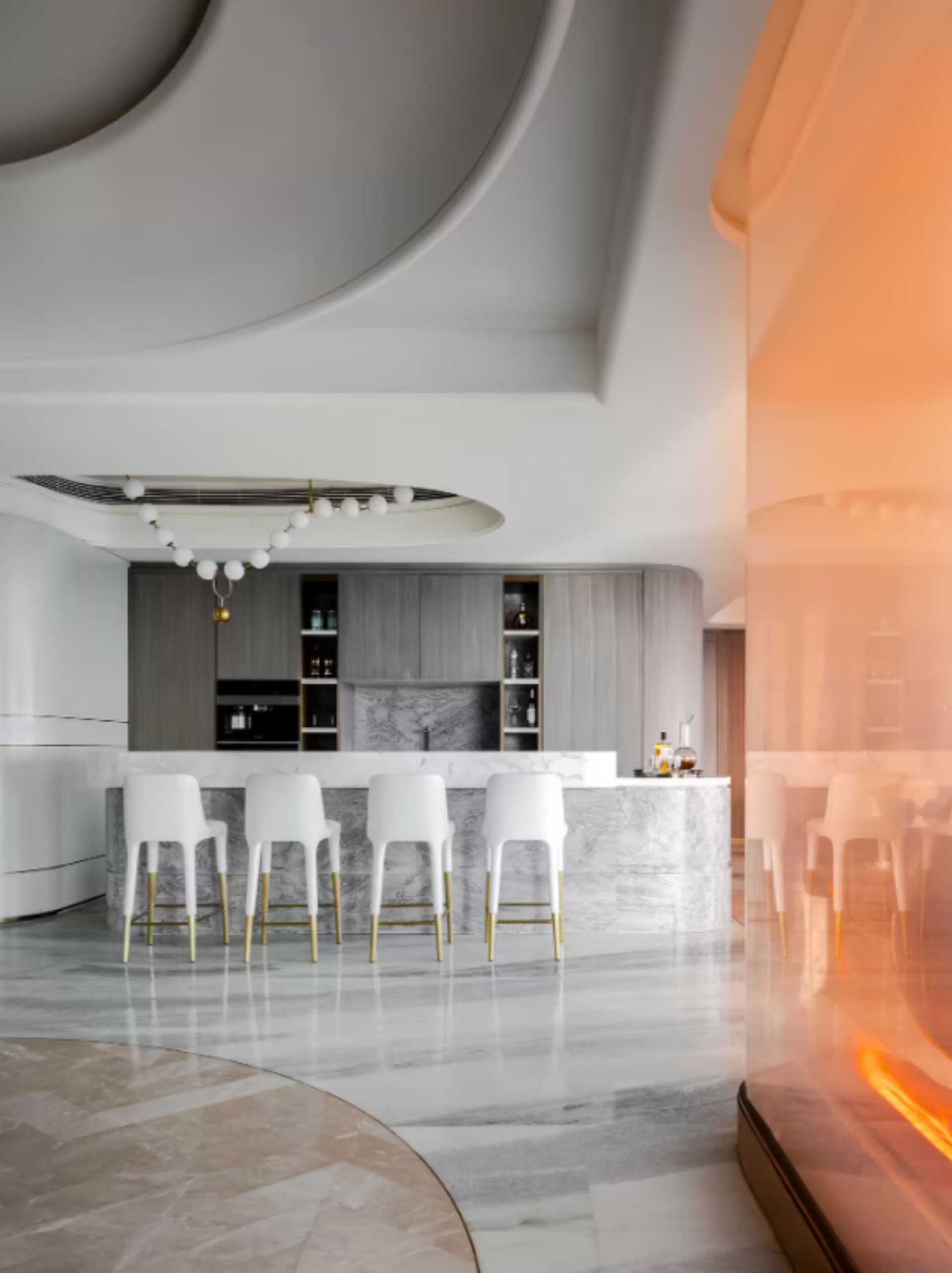 Modern kitchen featuring marble countertops and flooring, with white chairs and a minimalist design.
