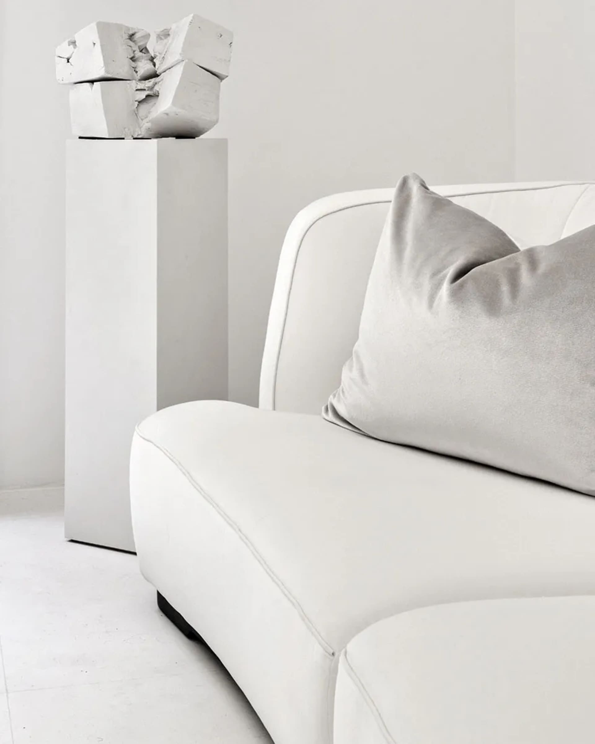 Contemporary living room with a modern white couch, grey throw pillows, and a geometric concrete sculpture