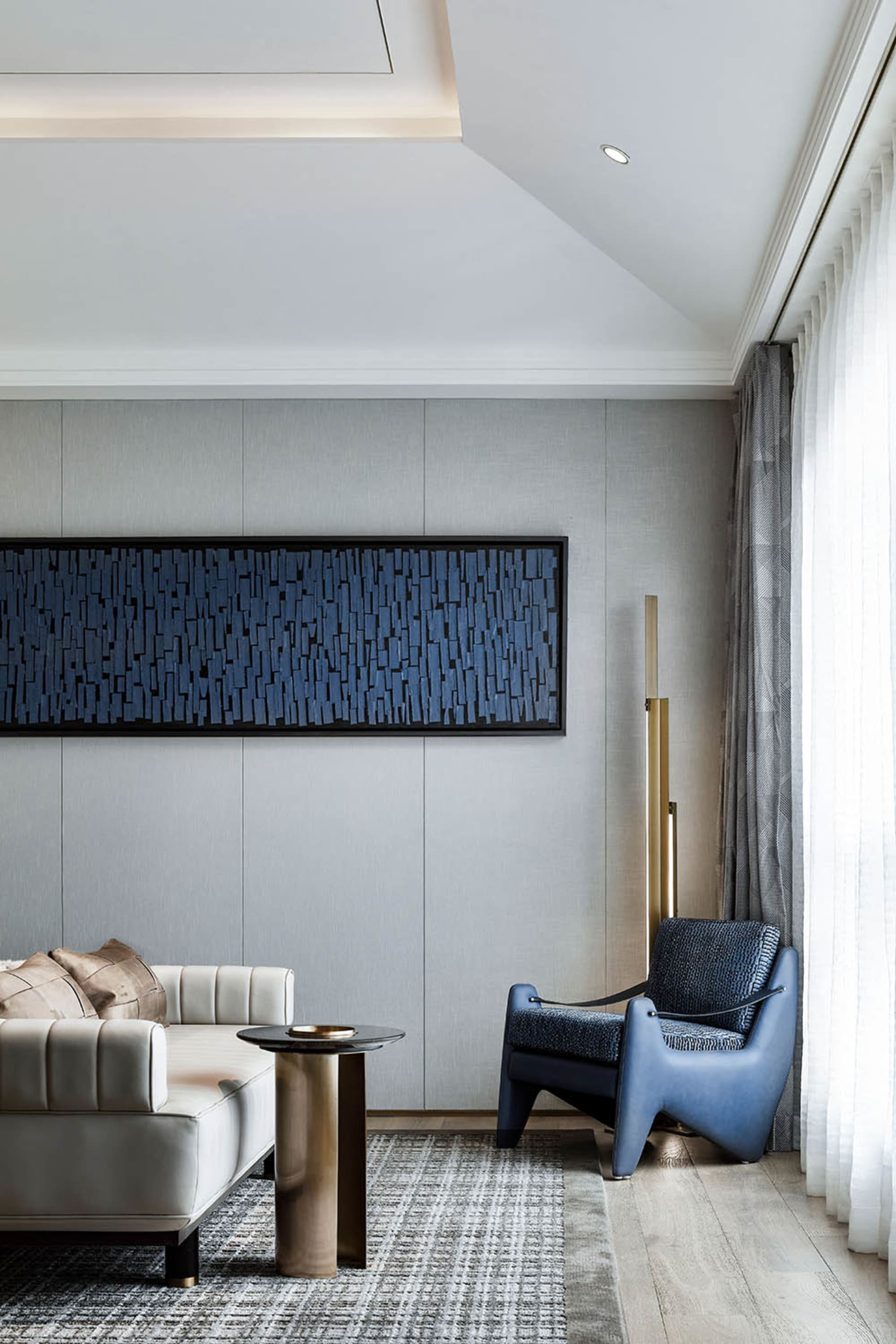A modern living room featuring a fabric wall art piece and a combination of furniture with a blue accent chair and a white so