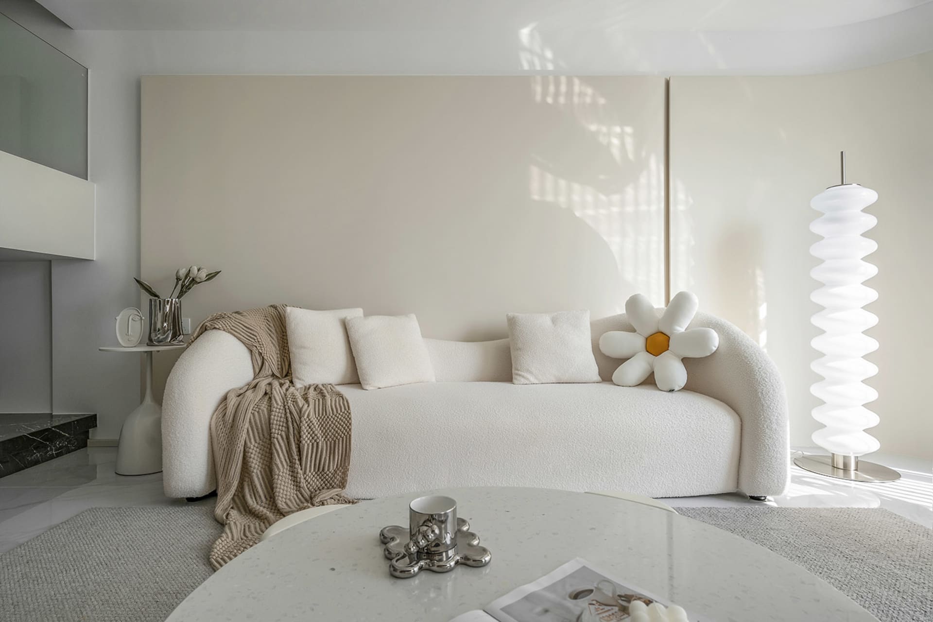 A minimalist living room with a white fabric sofa, cushions, and a round table.