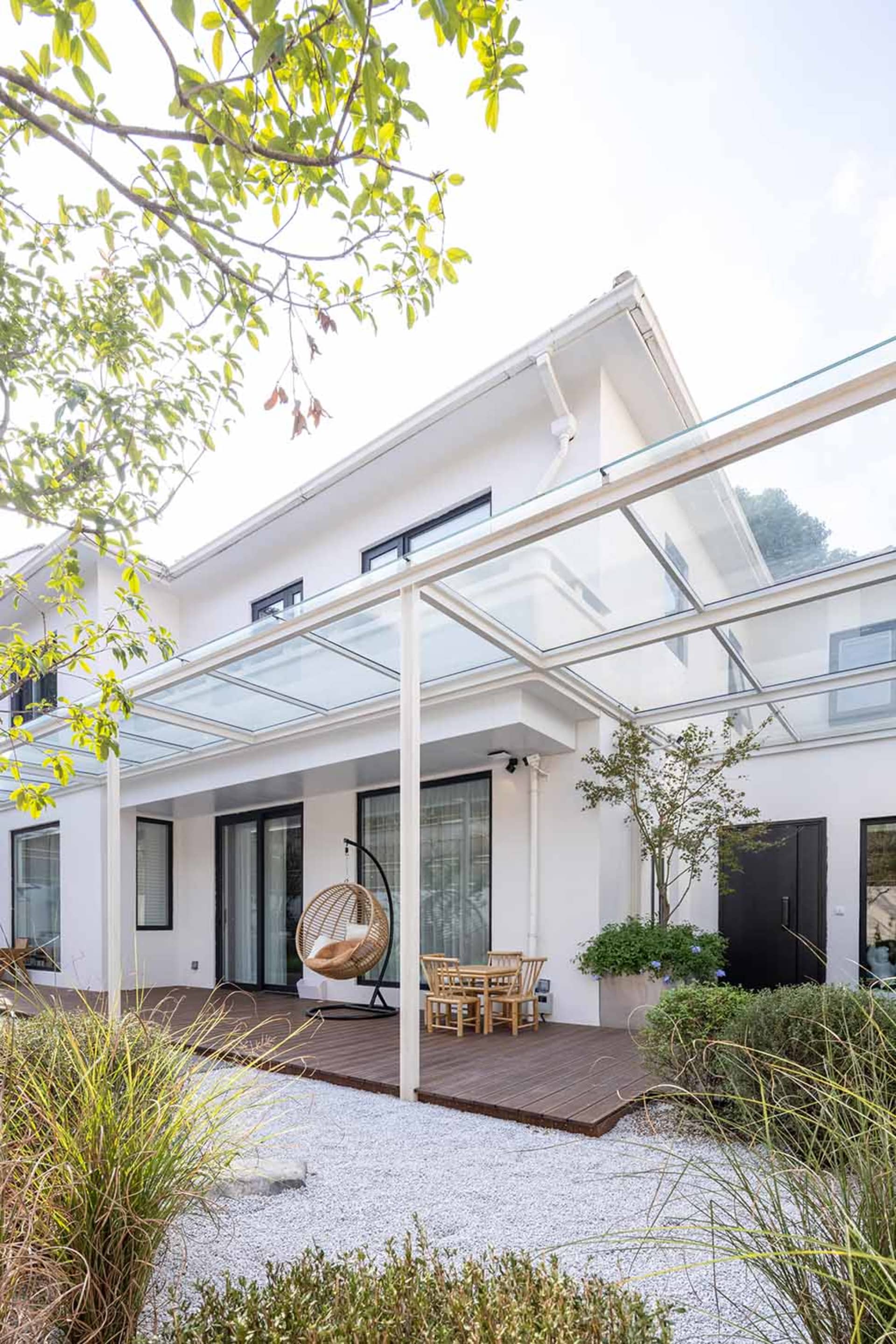 Modern patio with a glass roof and wooden deck, featuring minimalist design elements.