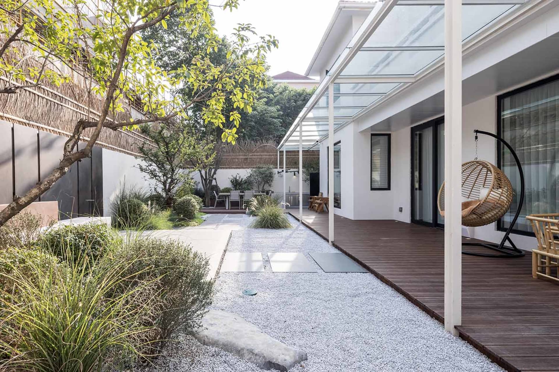 A modern residential exterior featuring a glass roof, white stone pavement, and wooden flooring.