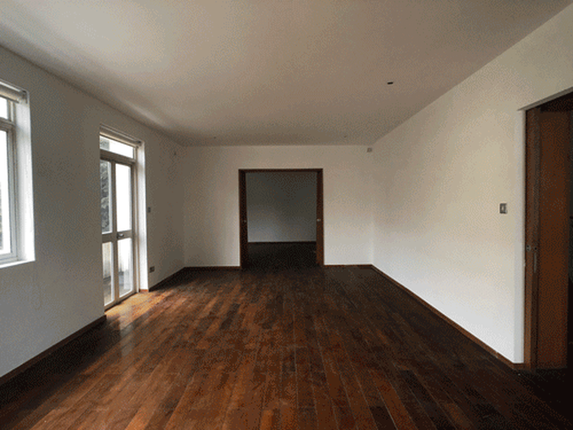 An empty room with hardwood floors, white walls, and a single open doorway leading to another room.