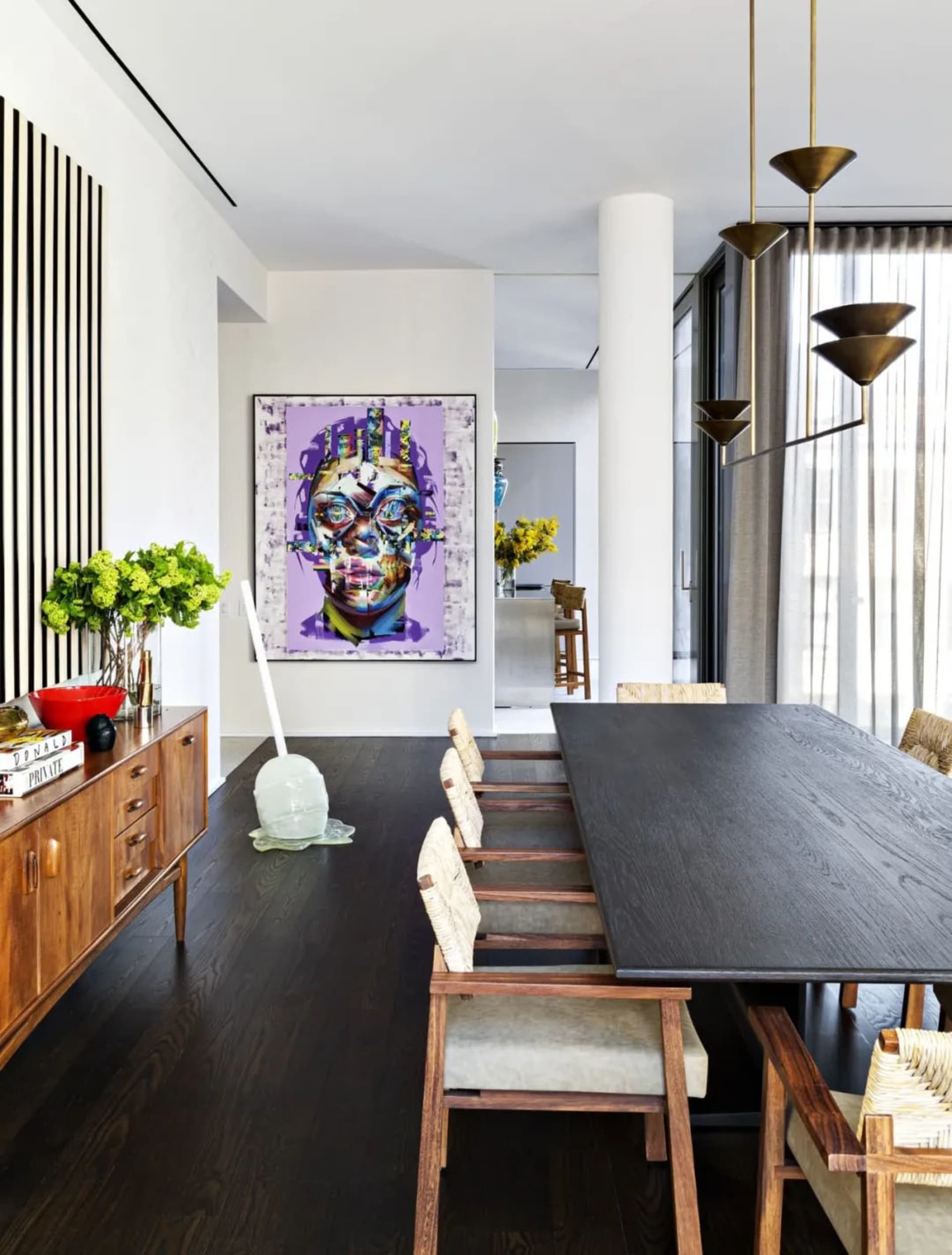 Modern dining room with a black wooden table, white cushioned chairs, and a colorful face painting.