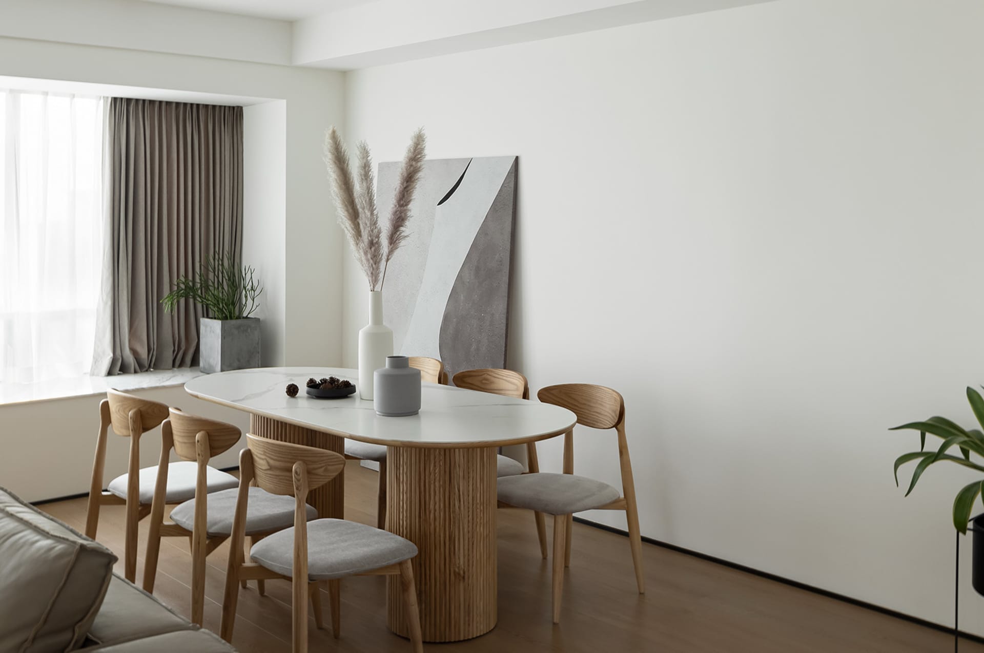 Modern living room featuring a marble and wooden dining table, wooden chairs with grey cushions, and abstract art on the wall